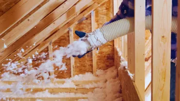 Person blowing loose insulation from an attic through a flexible hose during home insulation work