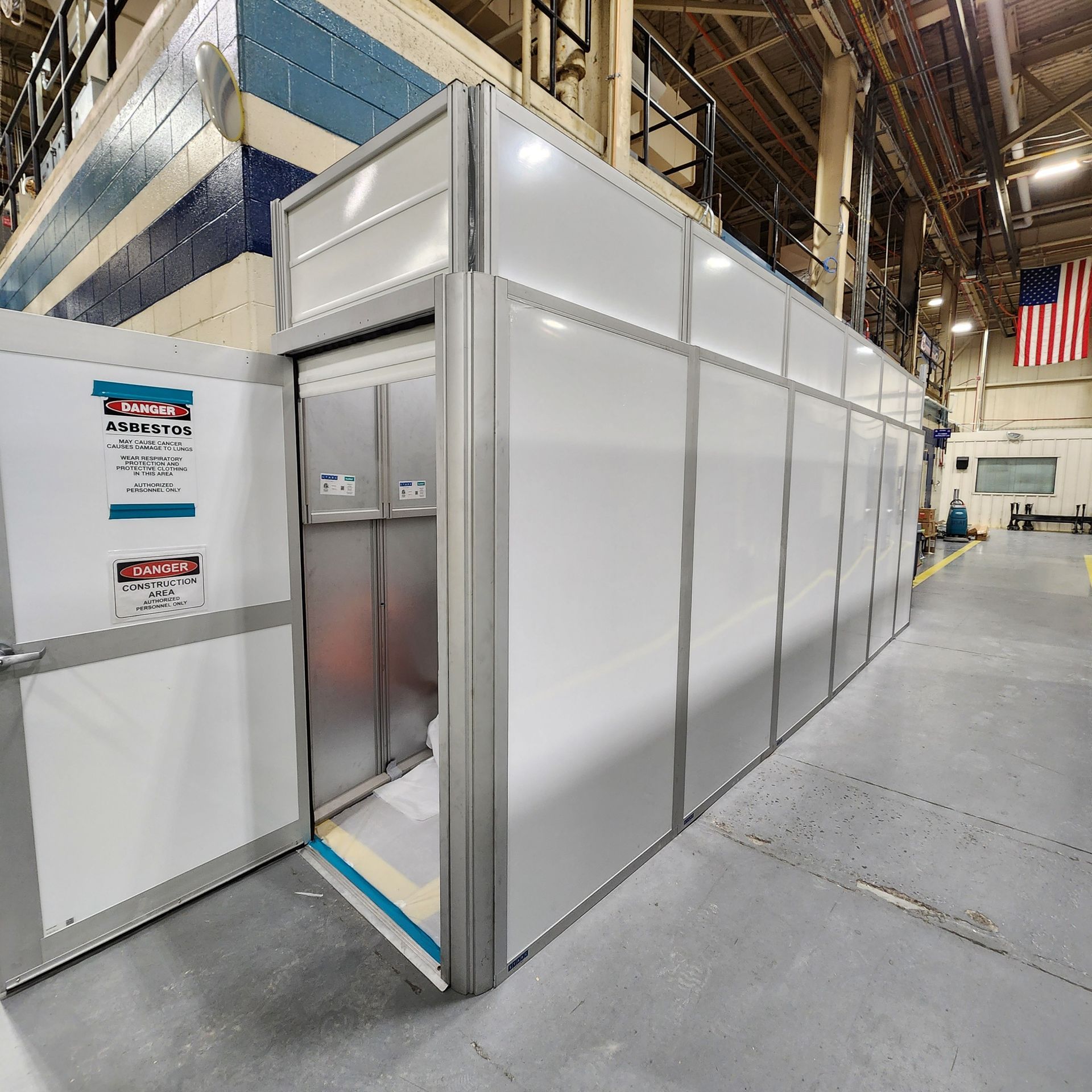 A white and metal containment enclosure in a factory setting, with an open door revealing equipment.