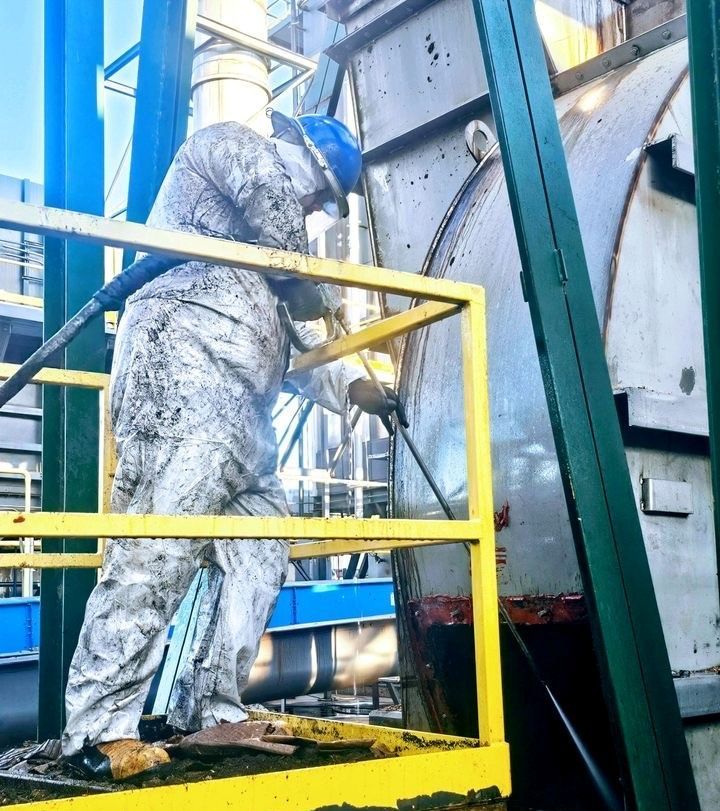 A industrial cleaning worker standing on a yellow railing working on a machine