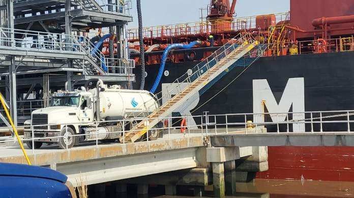 A large ship with the letter m on it is docked at a dock with First Environmental Vac truck