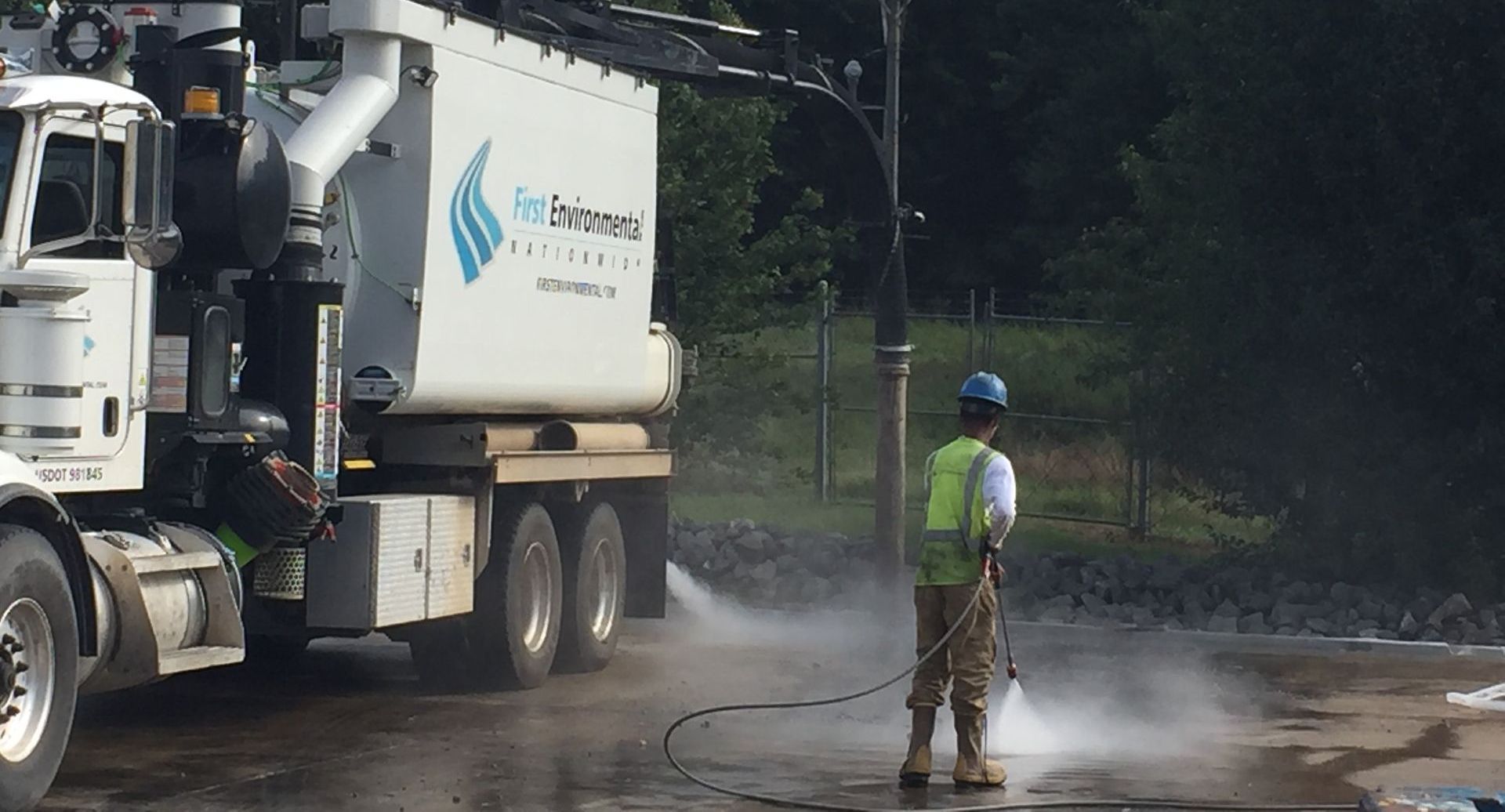 A man is pressure washing in front of a vacuum truck.