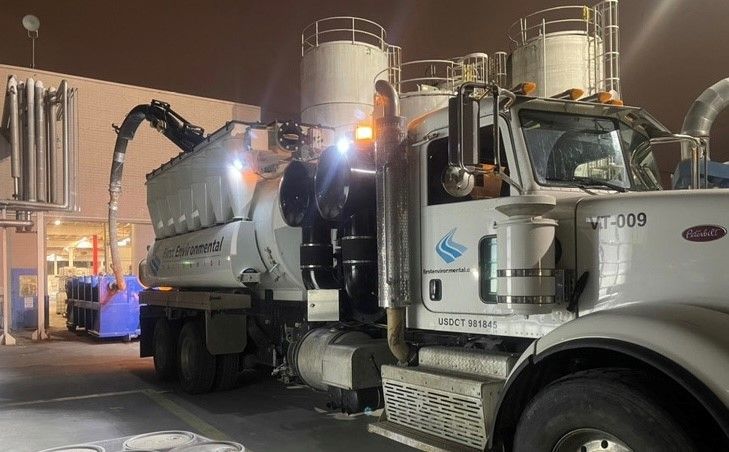 A vacuum truck is parked in front of a building at night.