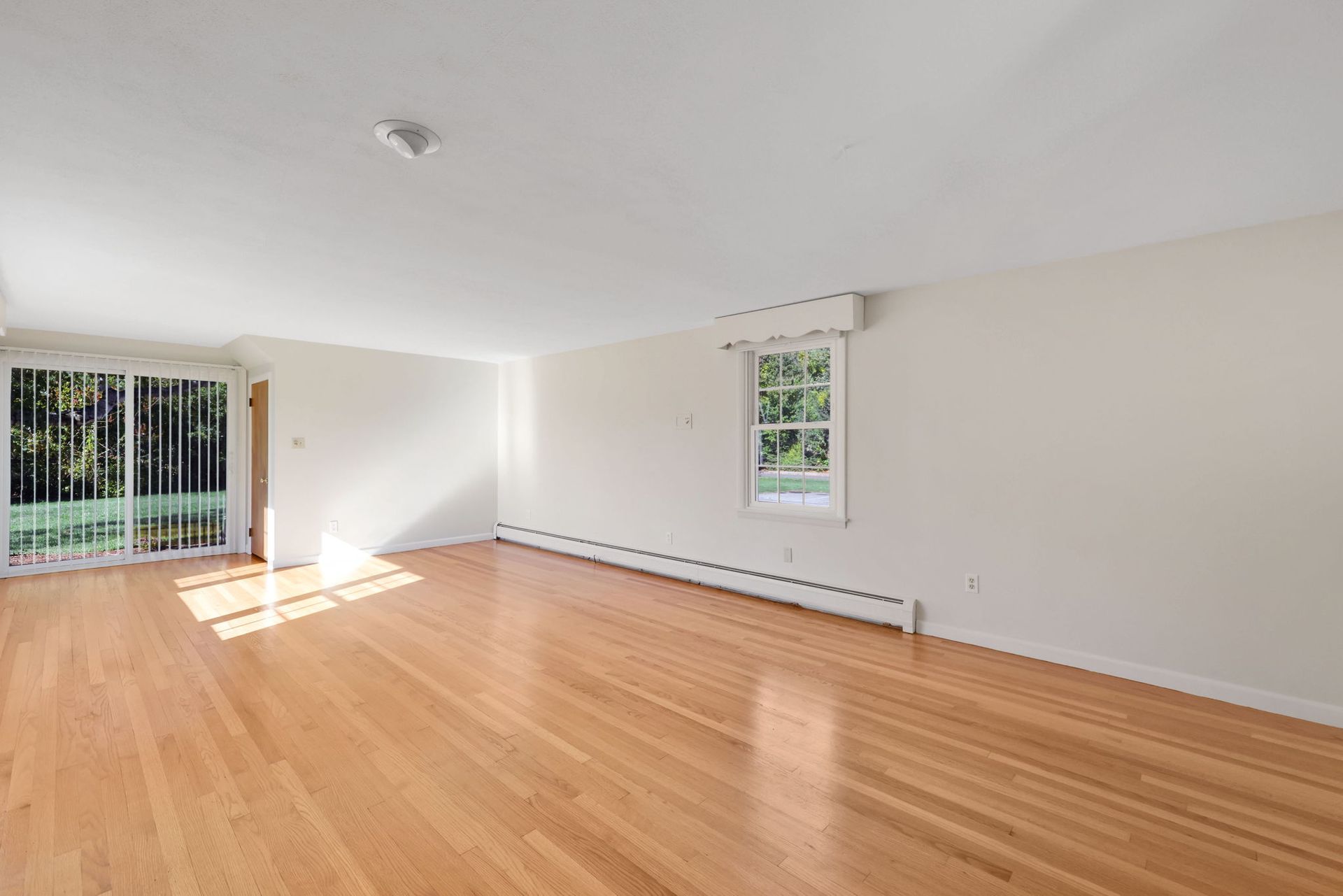 Empty room with wood floor, white walls and ceiling, sliding glass door, and small window.