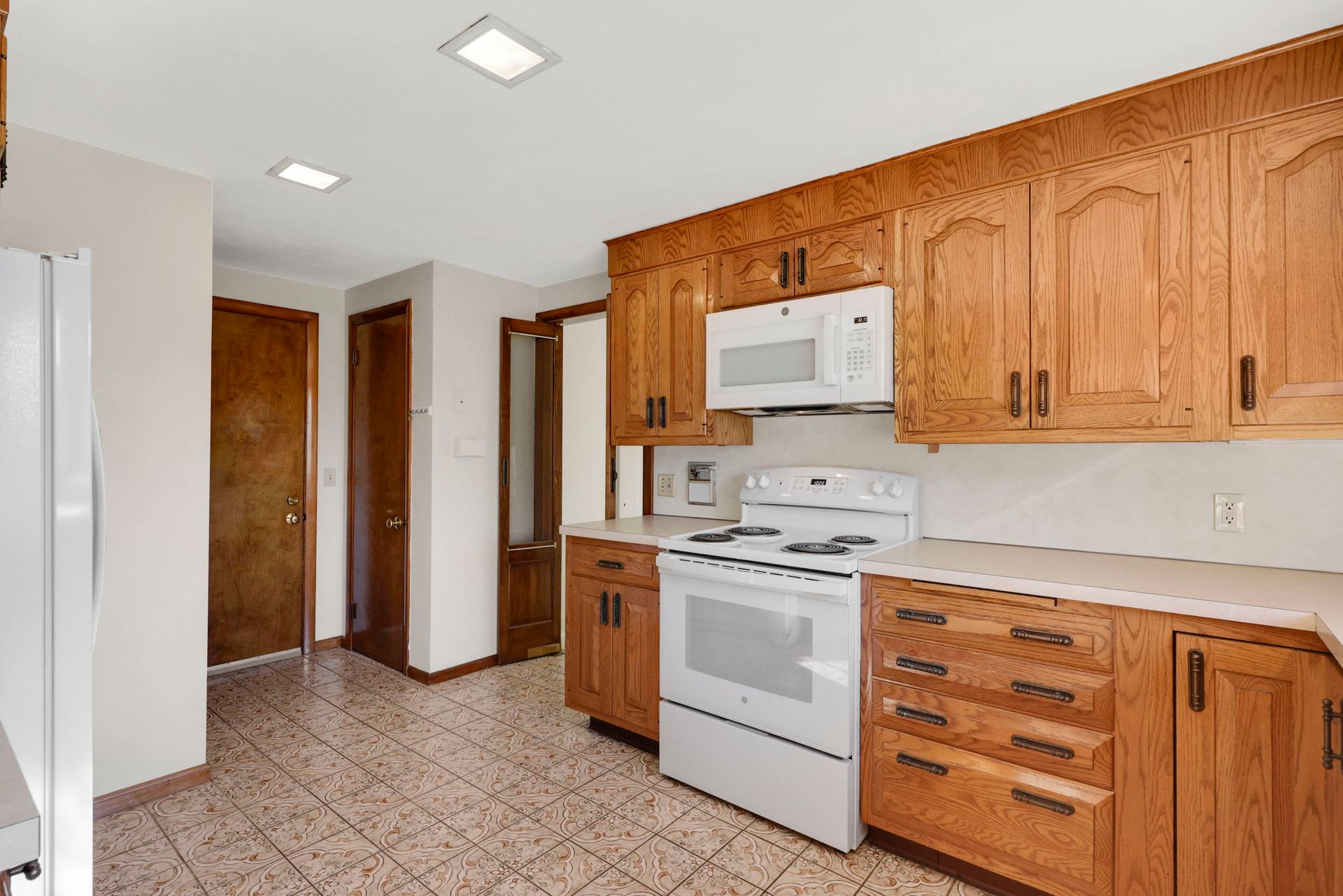 Kitchen with light-colored cabinets, white appliances, and tiled floor.