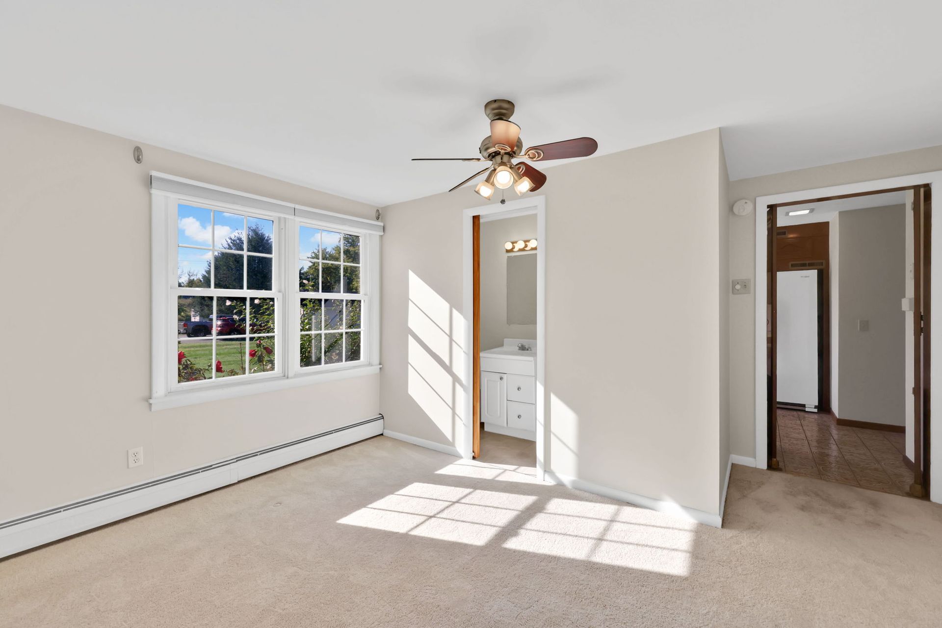Empty bedroom with large window, doorway to bathroom, and doorway to a hallway. Natural light.