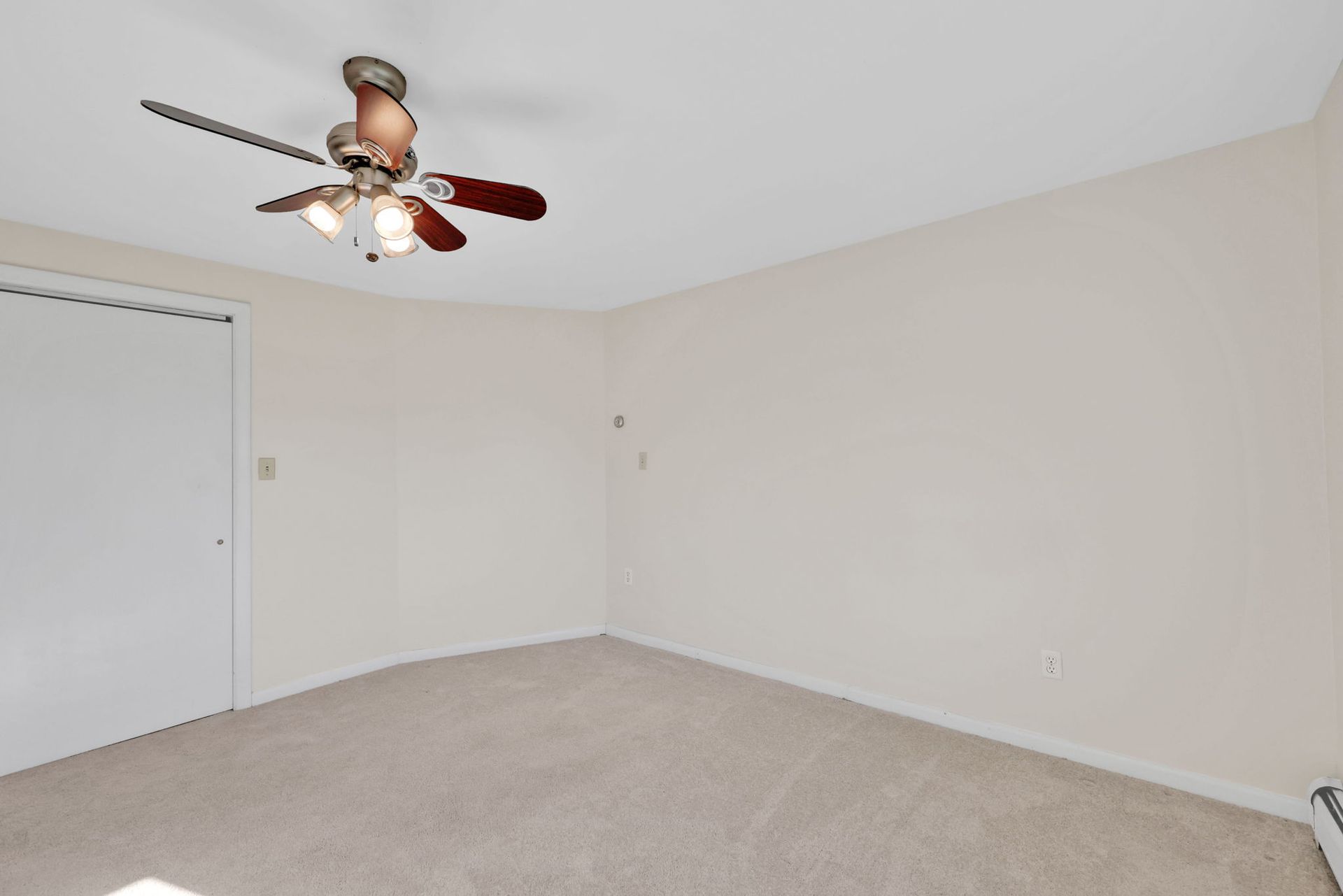 Empty room with beige carpet and walls, white door and ceiling fan.
