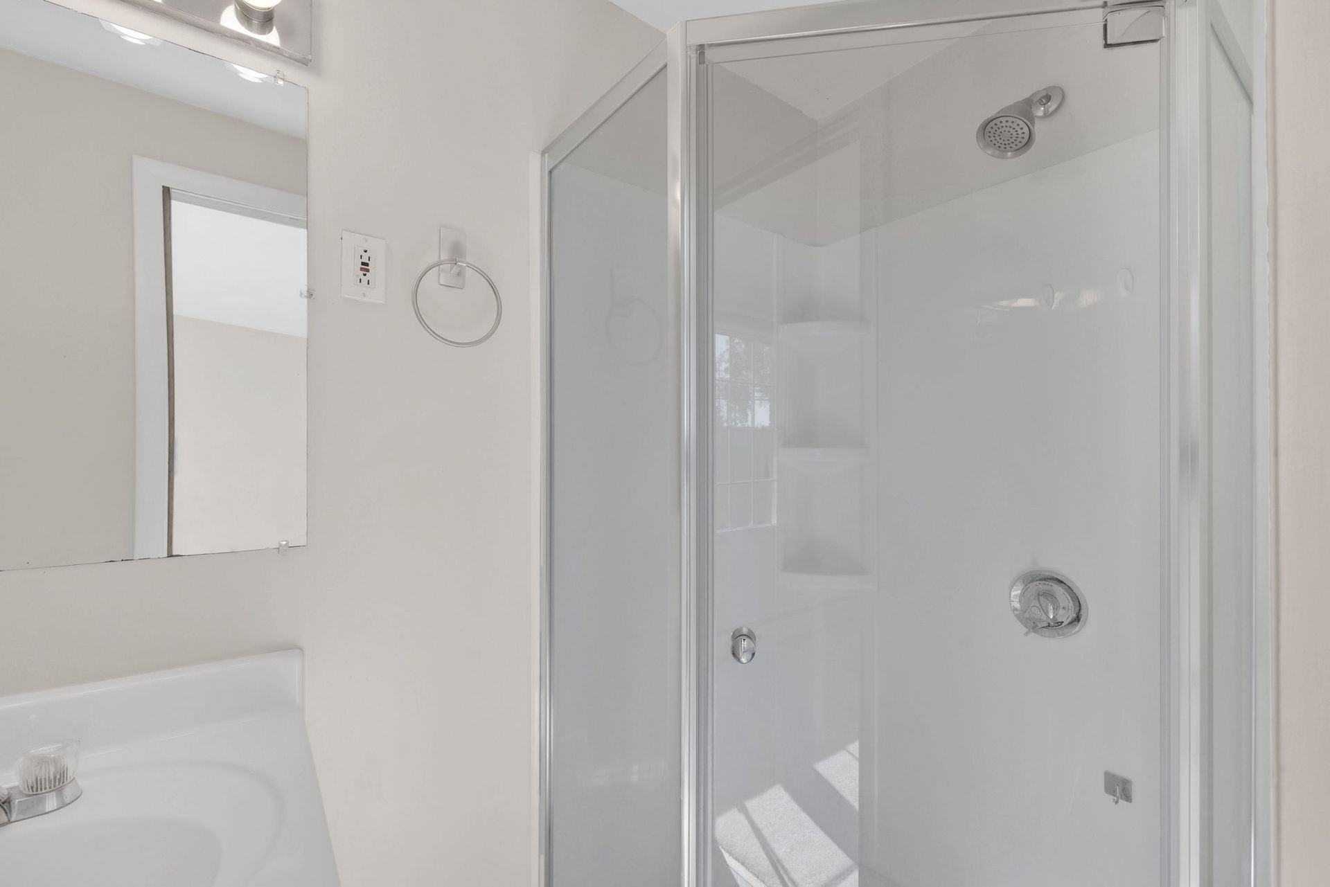 Bathroom with a white shower, sink, and mirror. White walls.