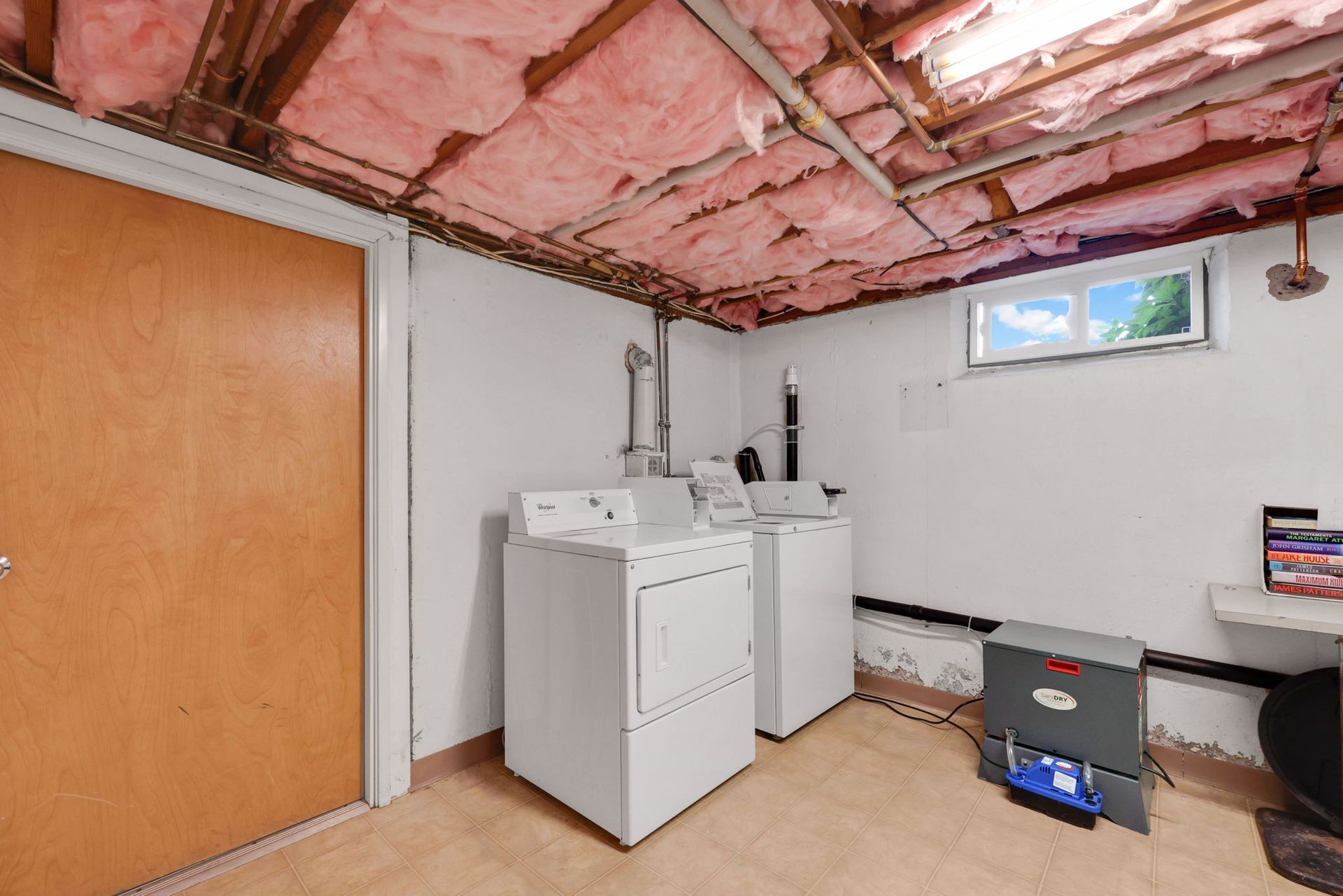 Laundry room with a washing machine, dryer, window, and exposed ceiling with pink insulation.