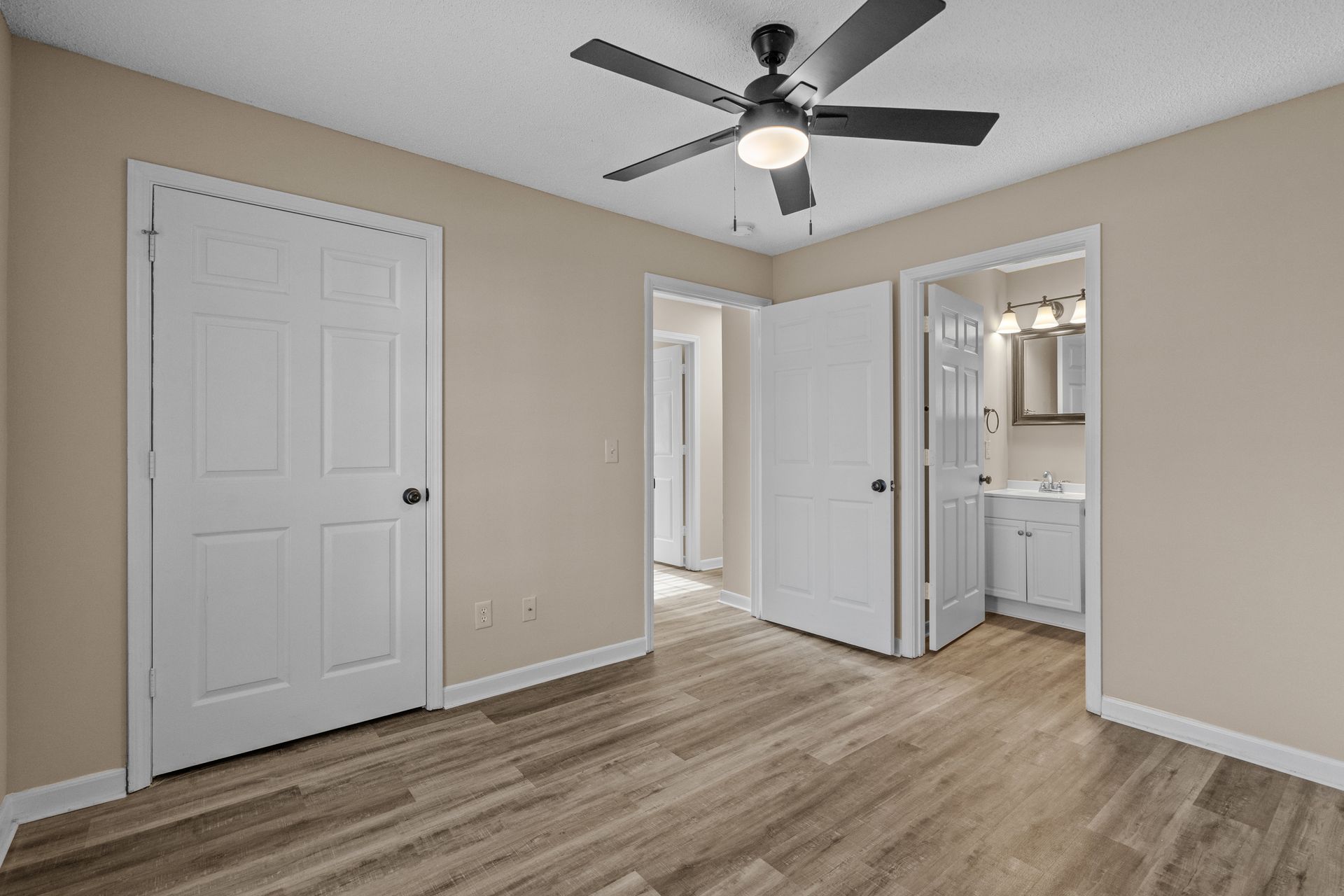 Bedroom with neutral walls, white doors, and wood-look flooring, with an open doorway to a bathroom.