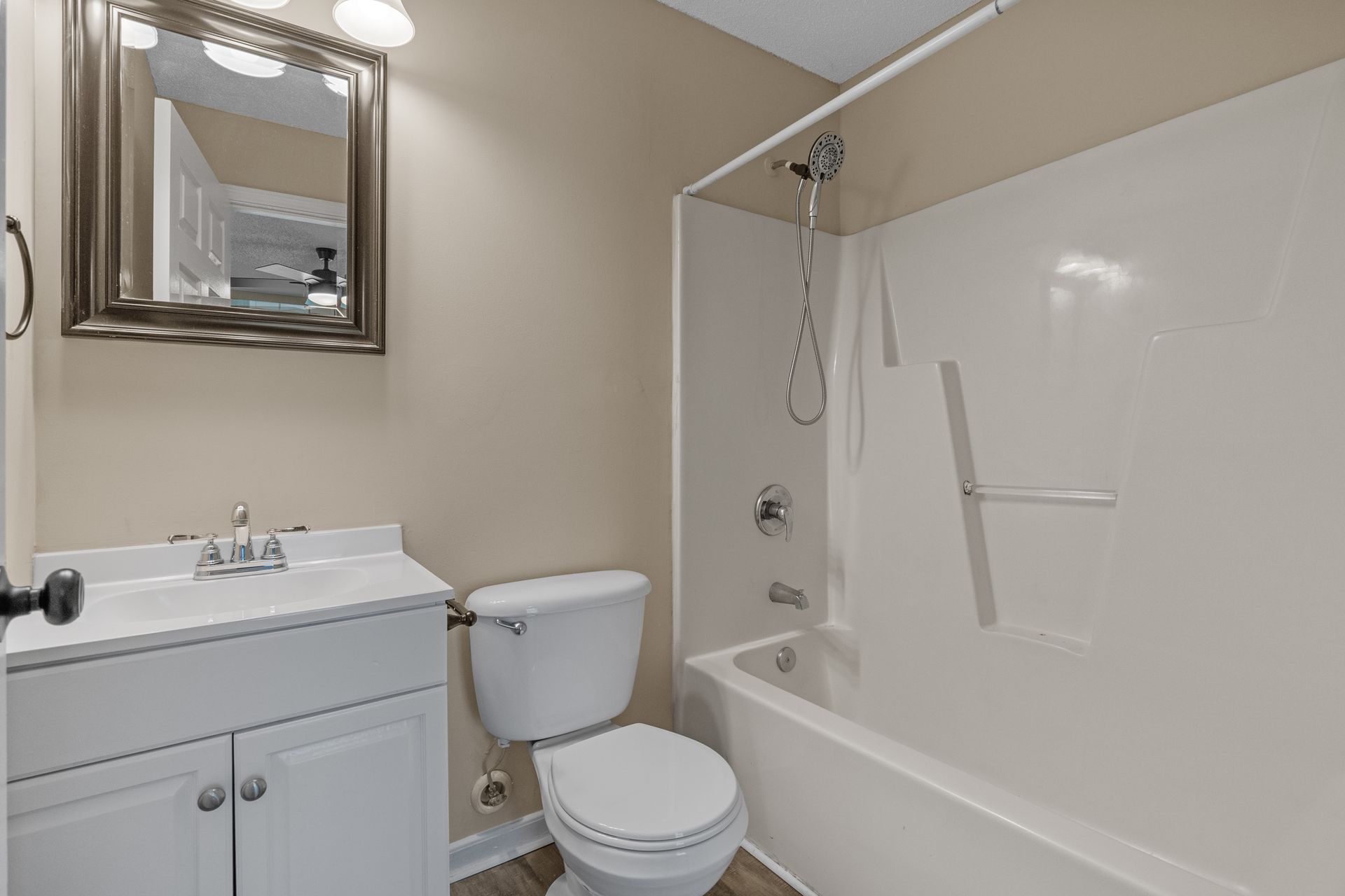 Bathroom with white fixtures, vanity, toilet, and bathtub. Neutral walls, decorative mirror.