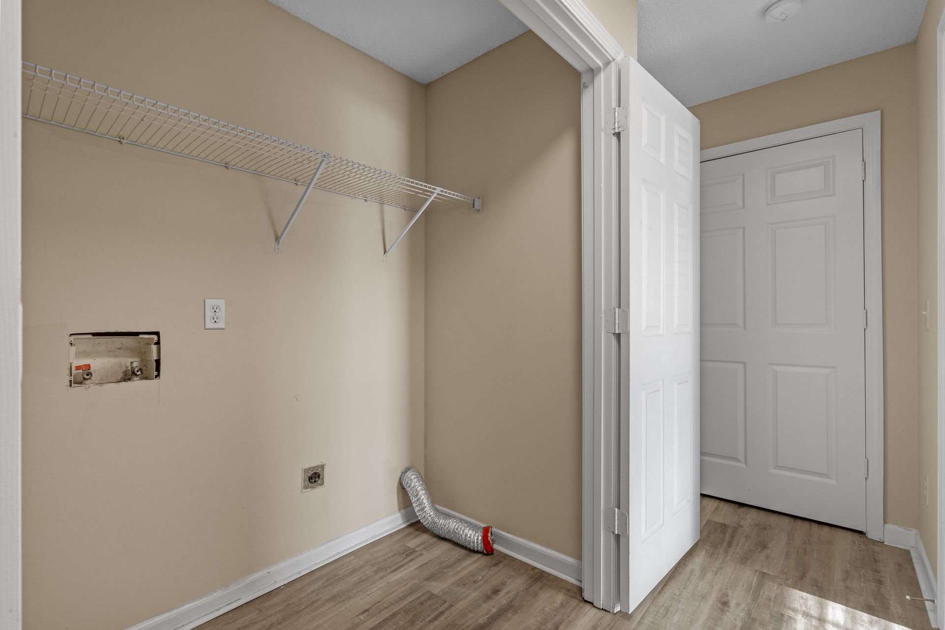 Empty laundry room with a wire shelf, beige walls, white doors, and wood-look flooring.