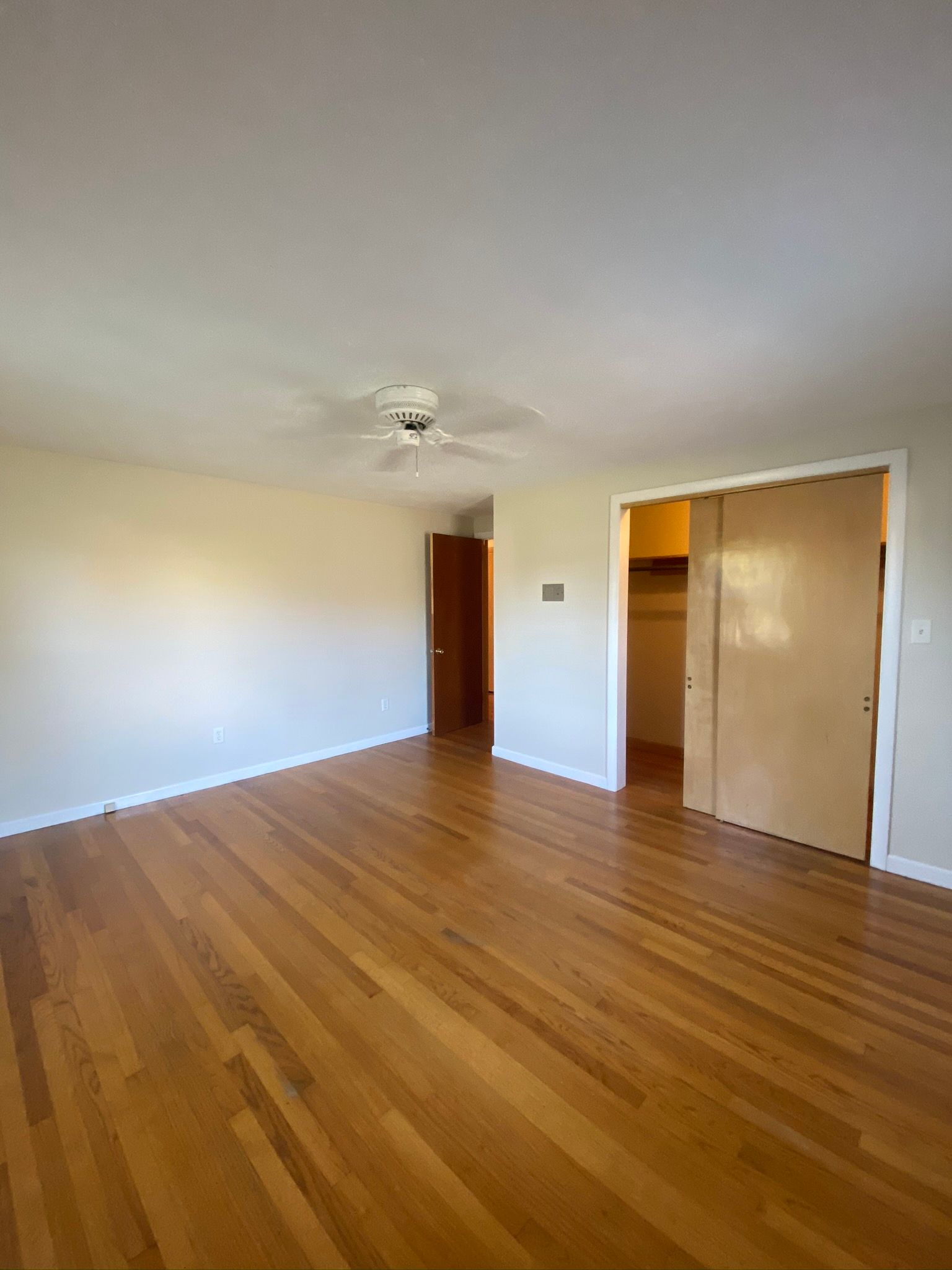 An empty living room with hardwood floors and a ceiling fan.