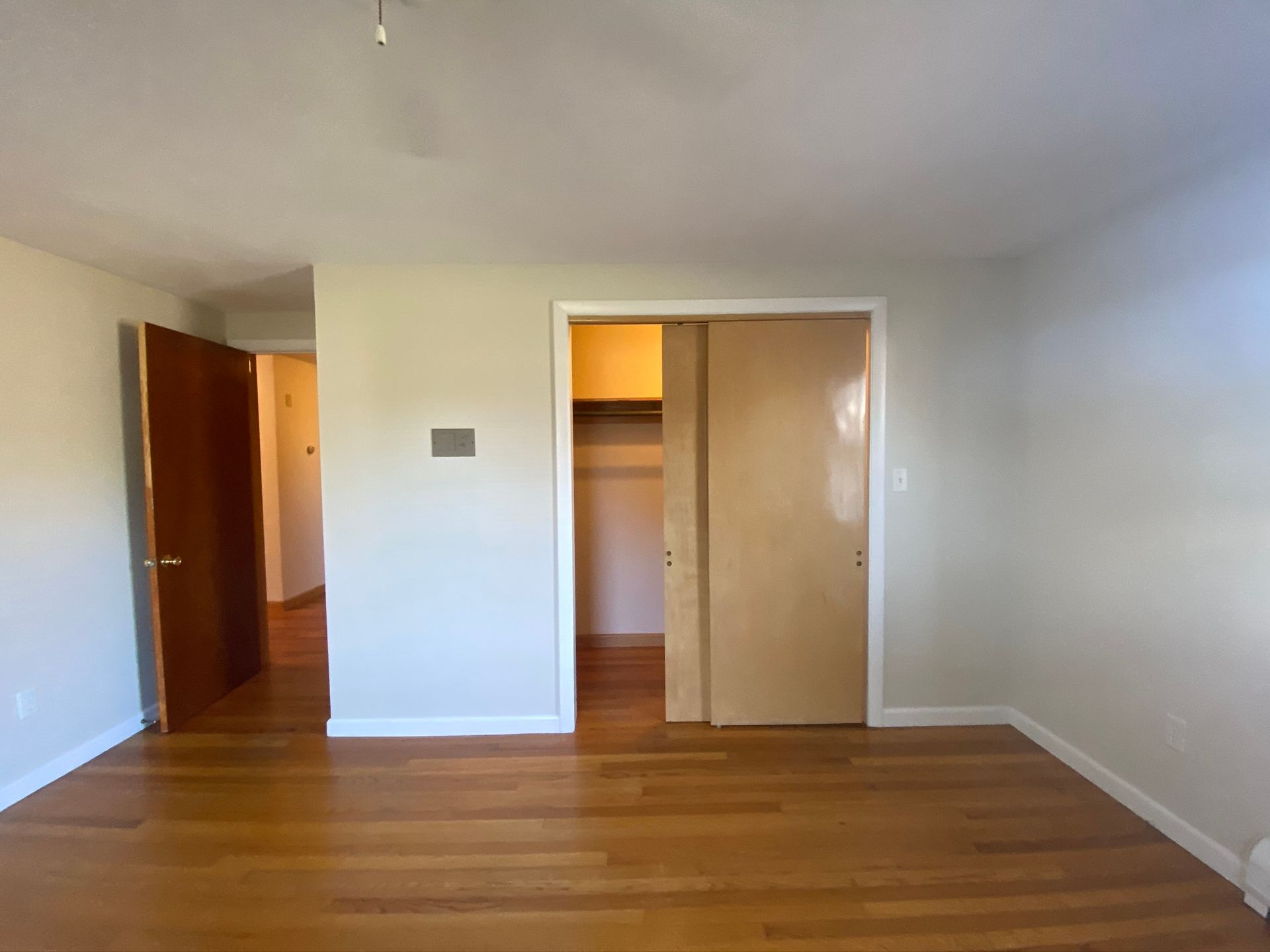 An empty bedroom with hardwood floors and a closet.