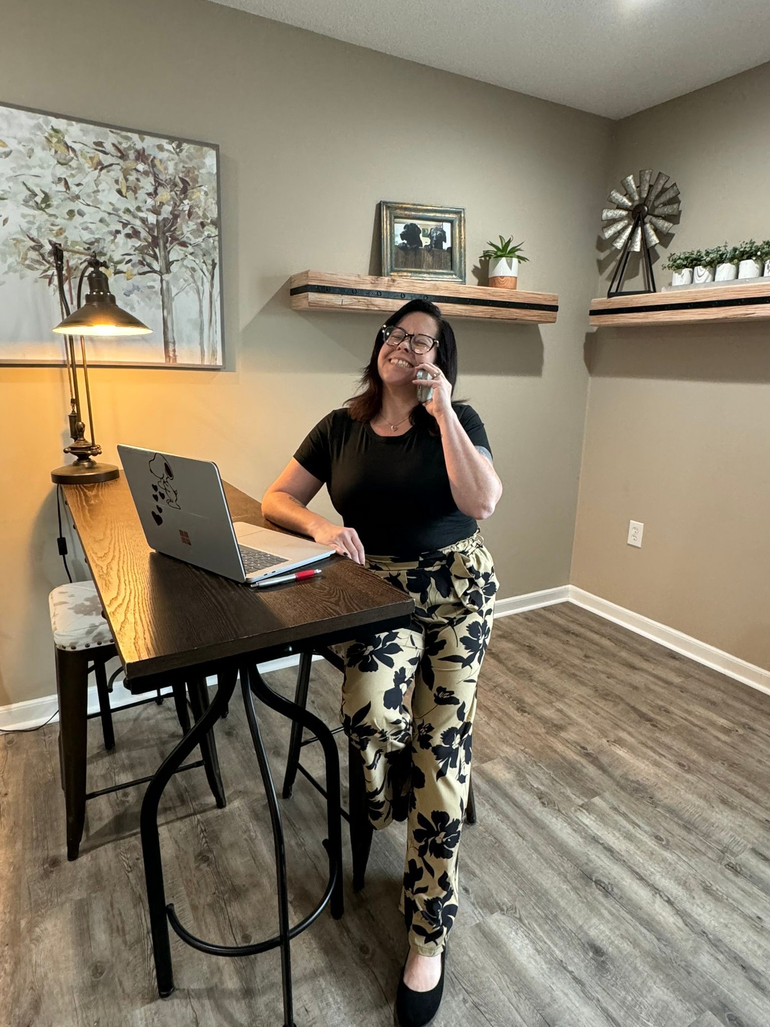A woman is sitting at a desk with a laptop and talking on a cell phone.