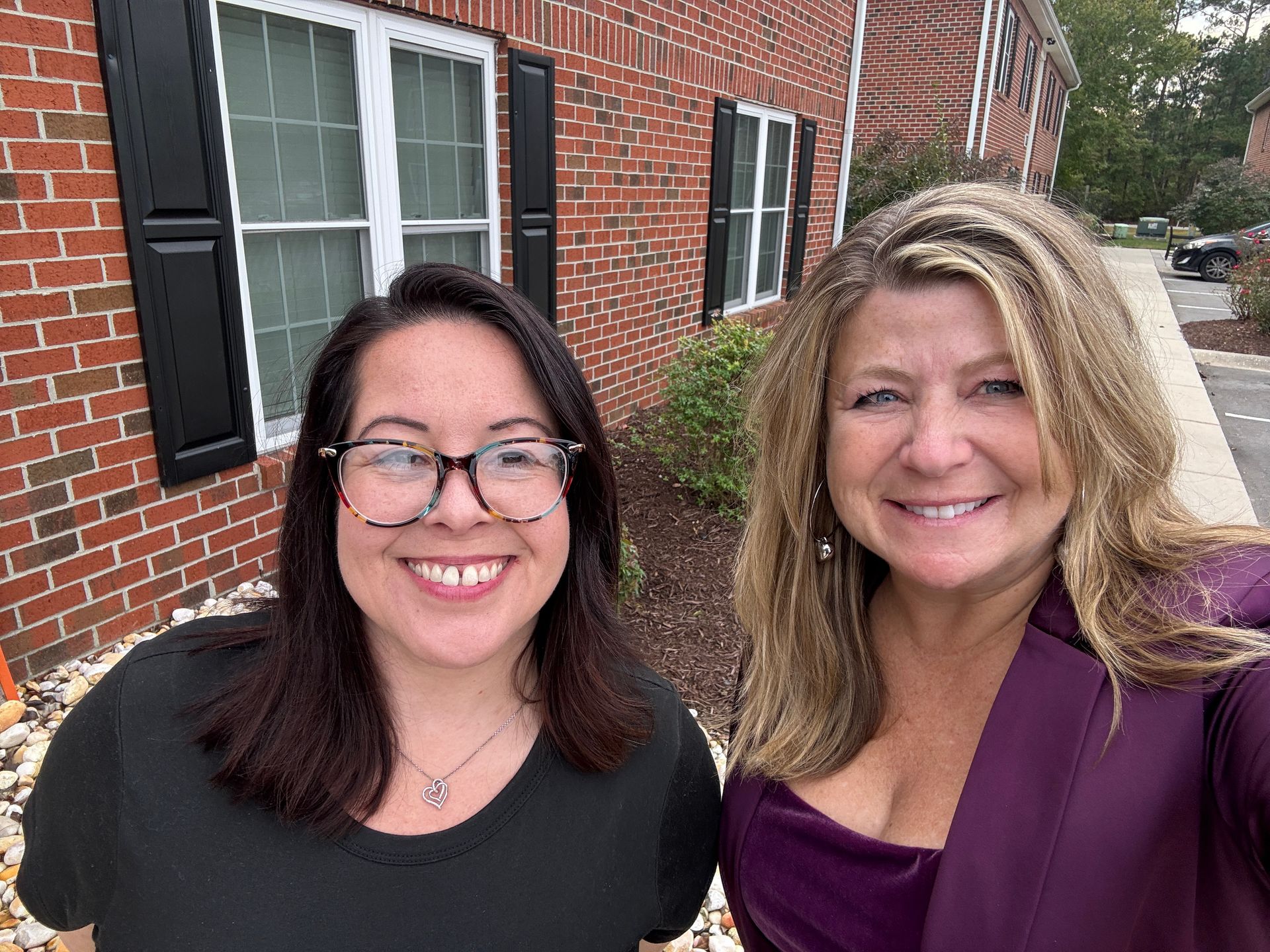 Two women are posing for a picture in front of a brick building.