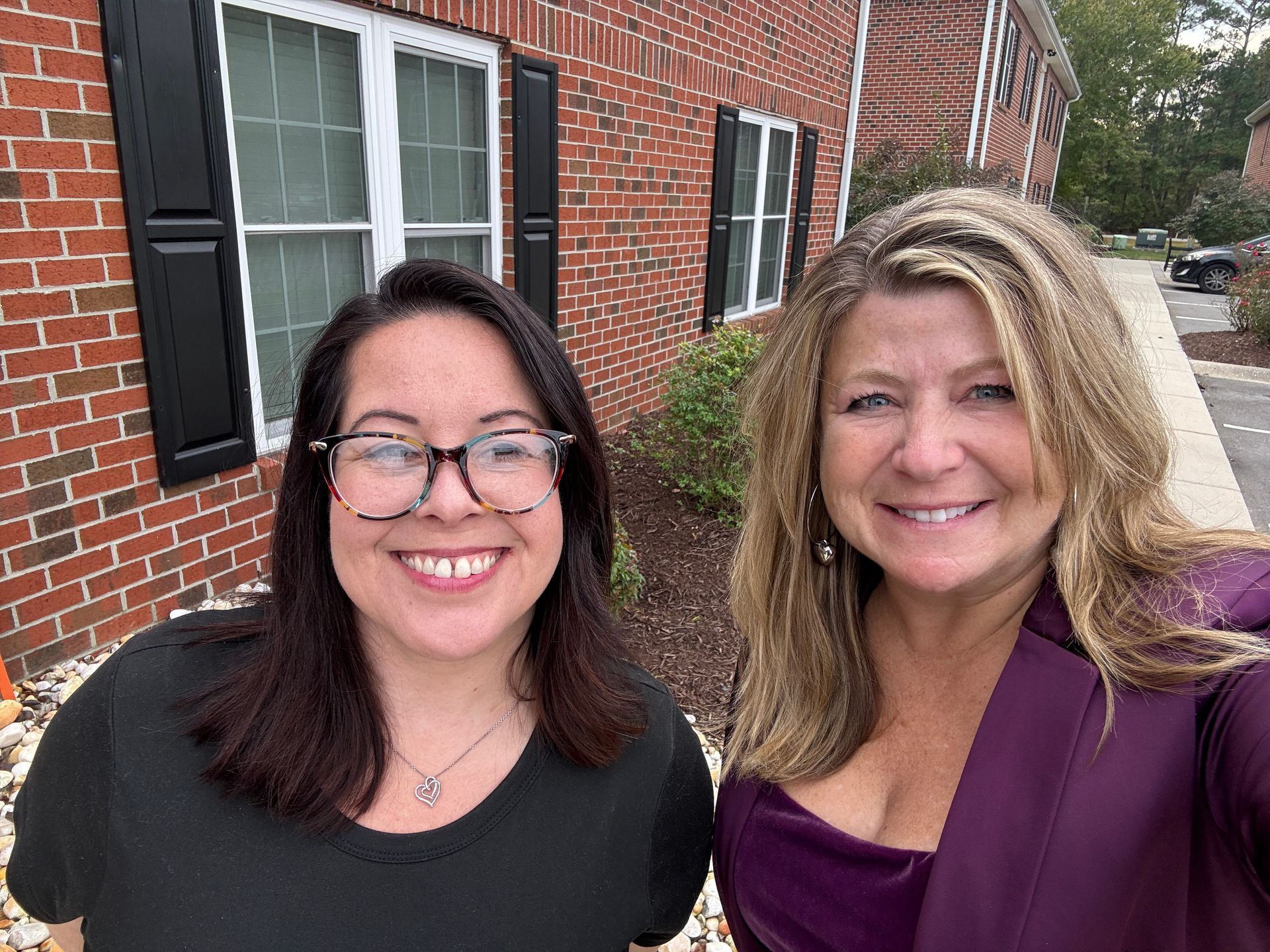 Two women are posing for a picture in front of a brick building.