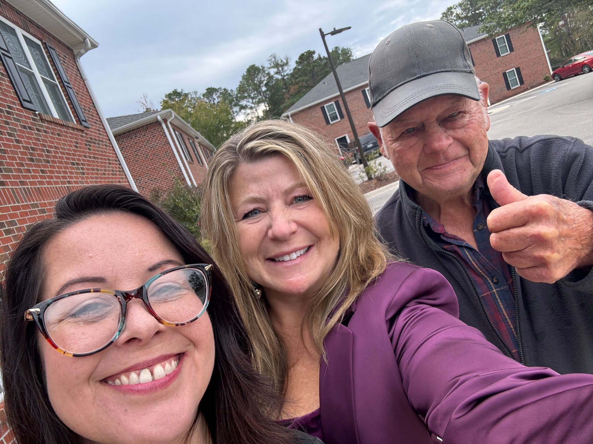 A man and two women are posing for a selfie and the man is giving a thumbs up.