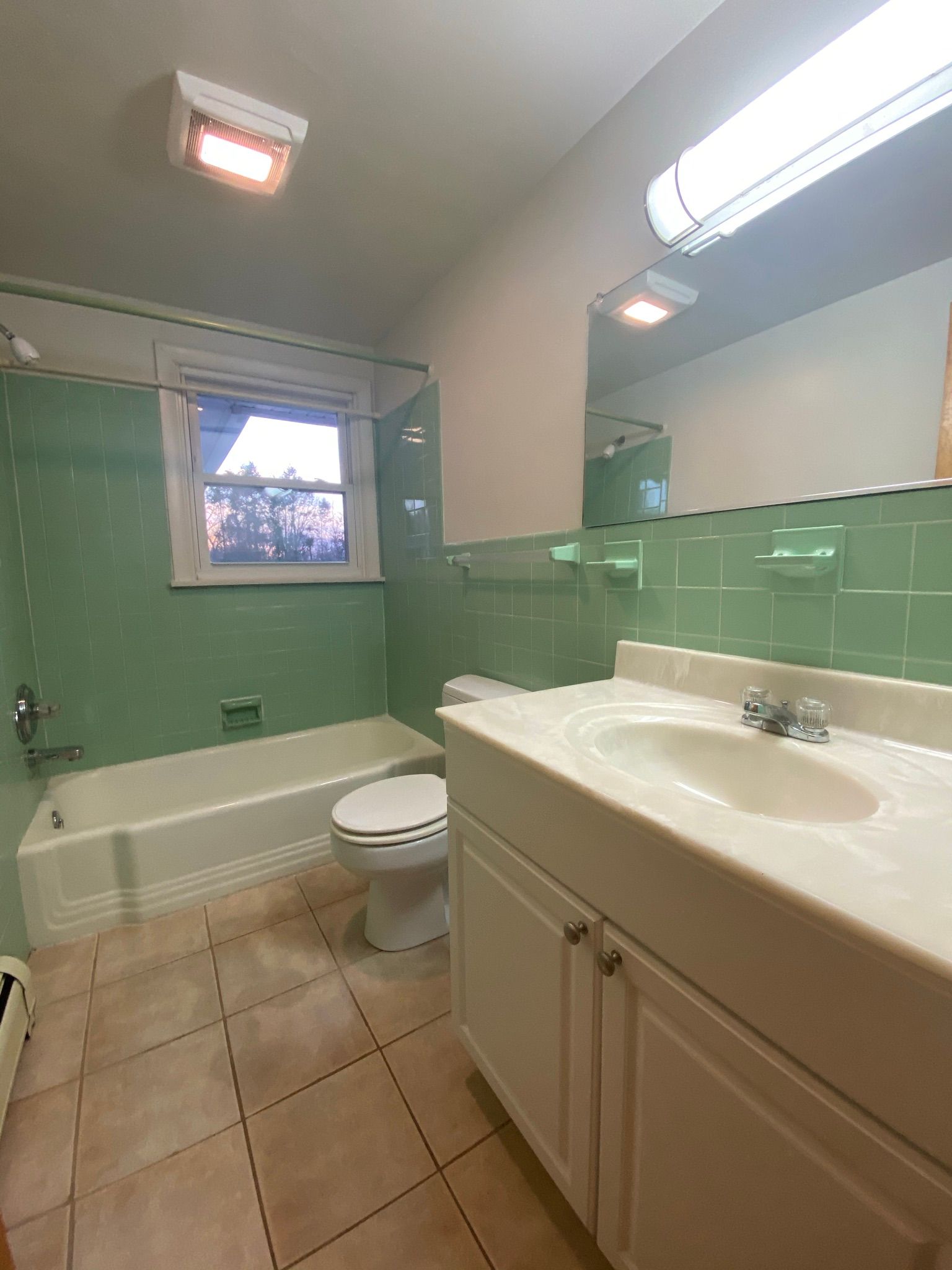 A bathroom with green tiles , a toilet , sink and bathtub.