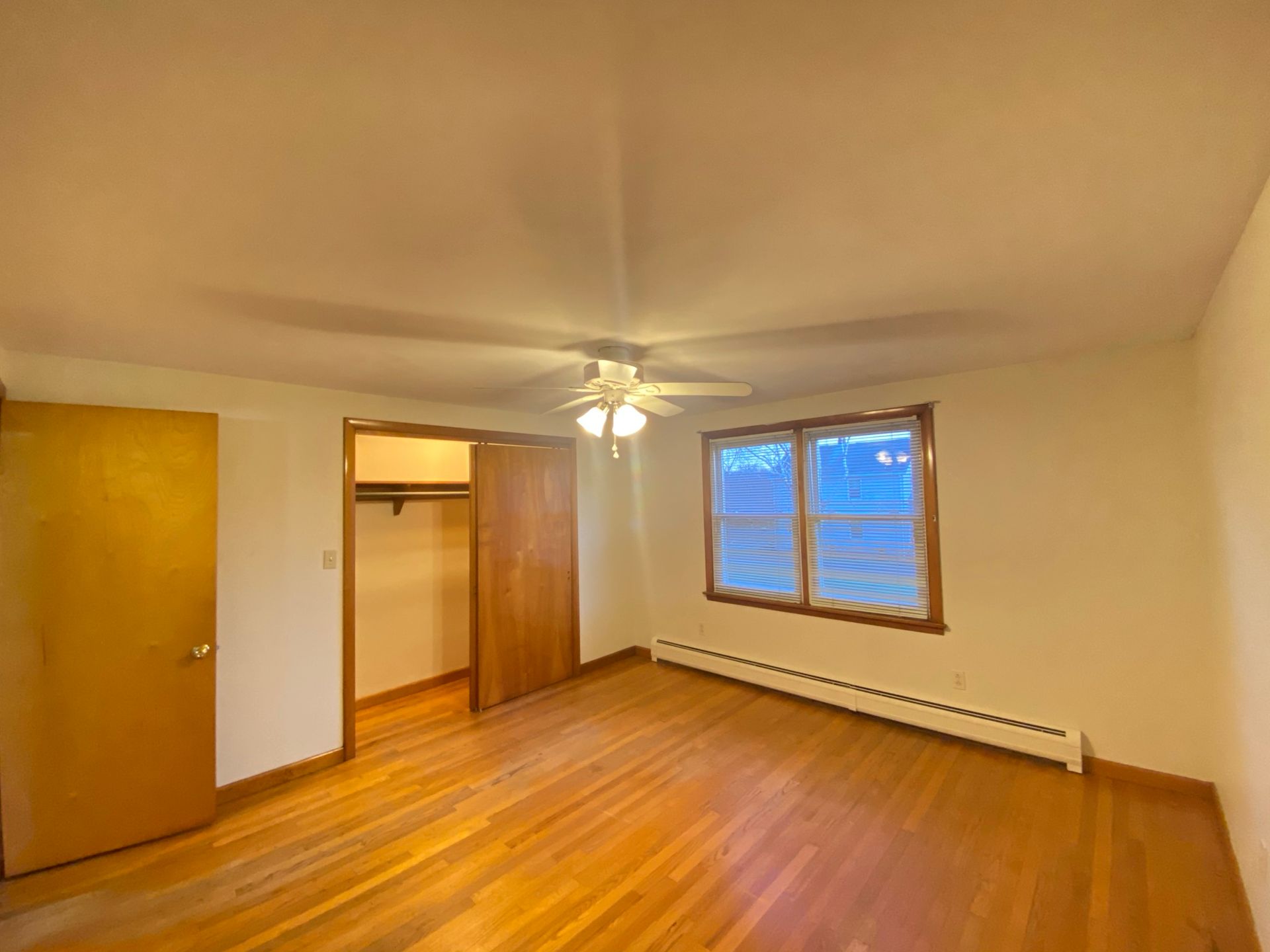 An empty bedroom with hardwood floors and a ceiling fan.