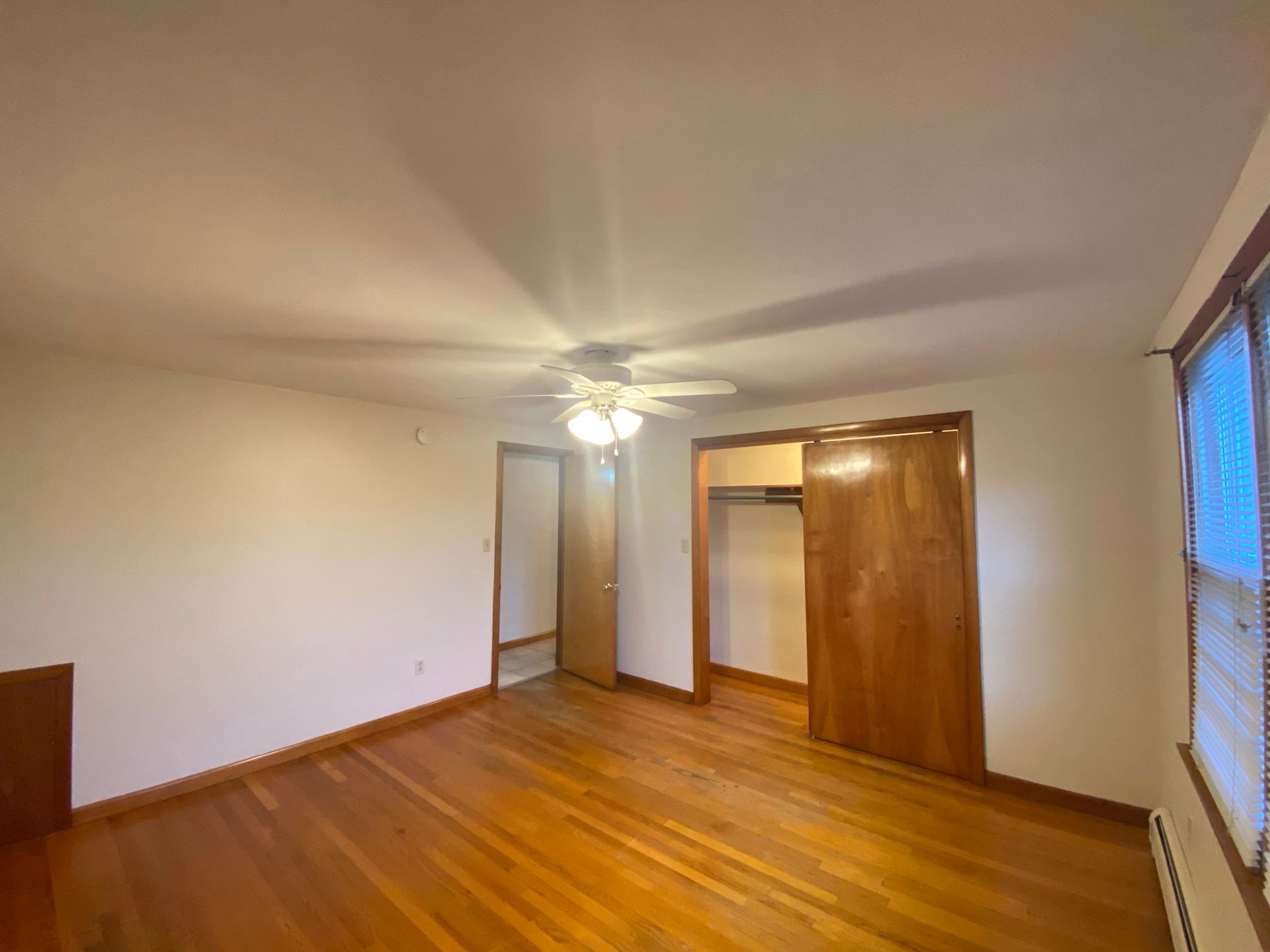 An empty bedroom with hardwood floors and a ceiling fan.