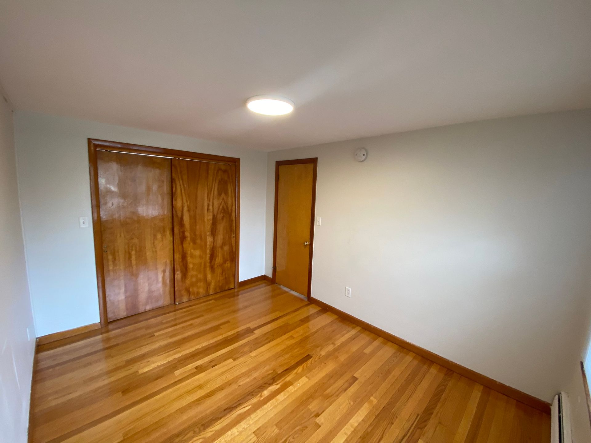 An empty room with hardwood floors and sliding doors.