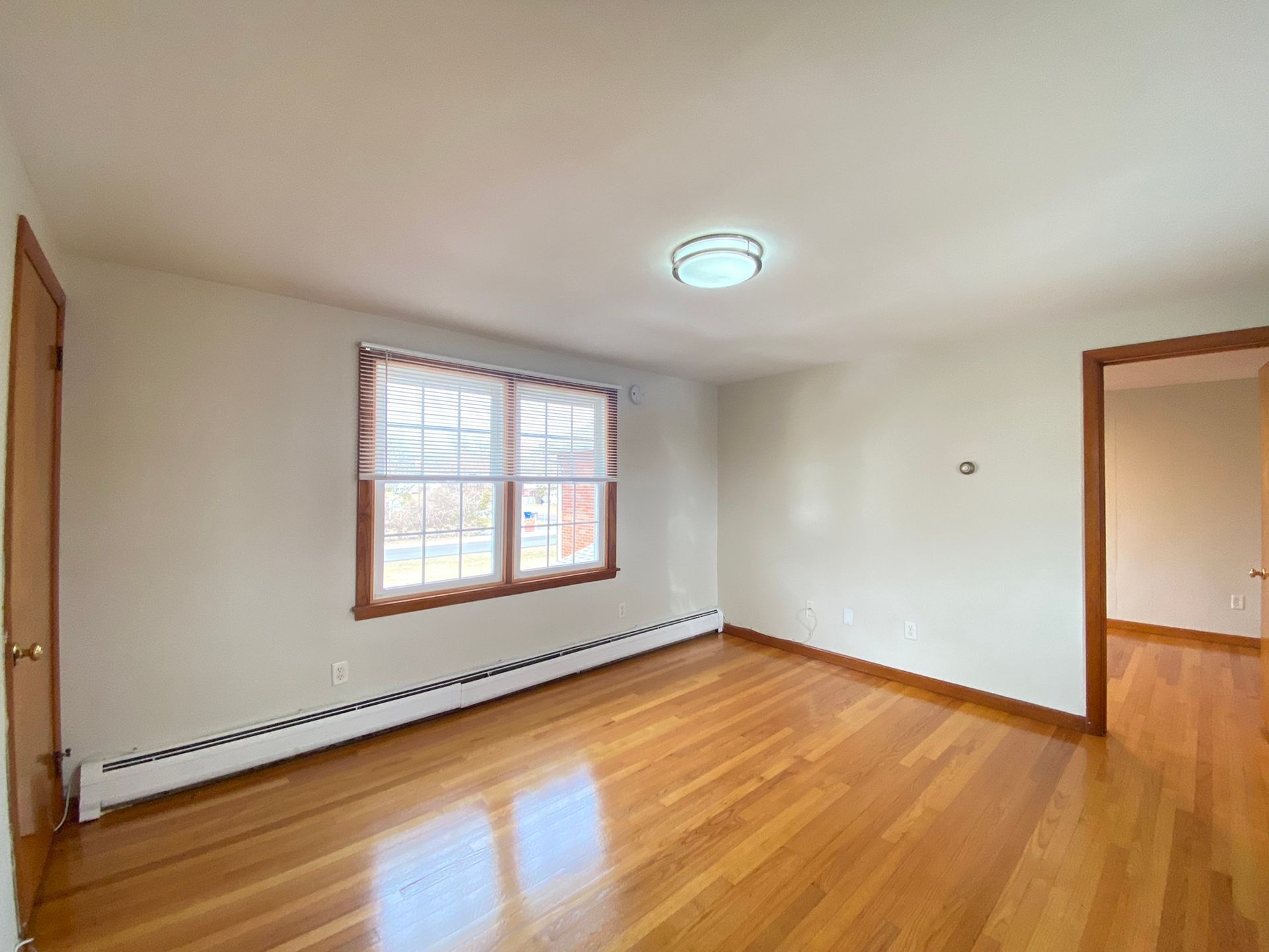 An empty living room with hardwood floors and two windows.