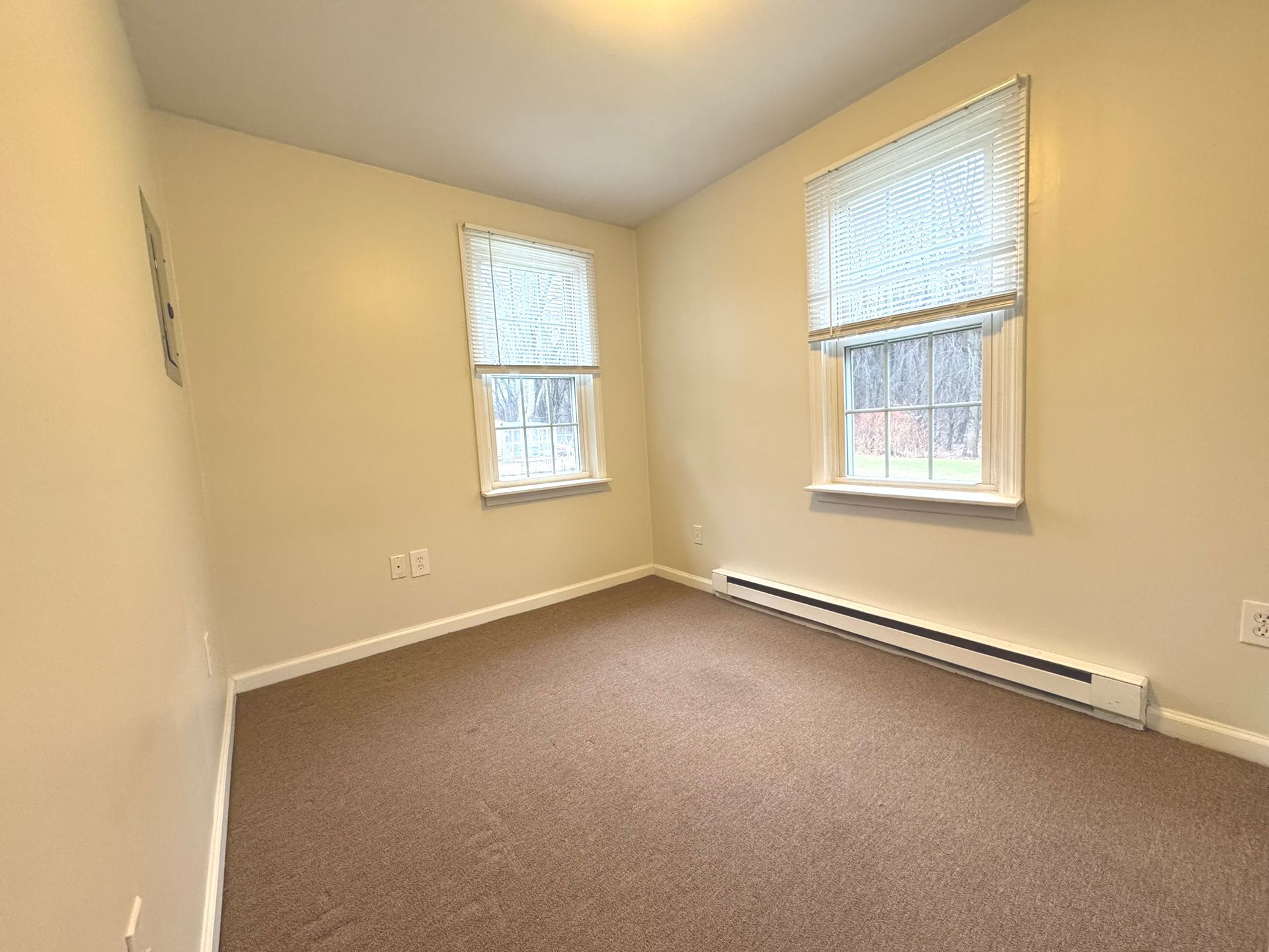 An empty bedroom with two windows and a brown carpet.