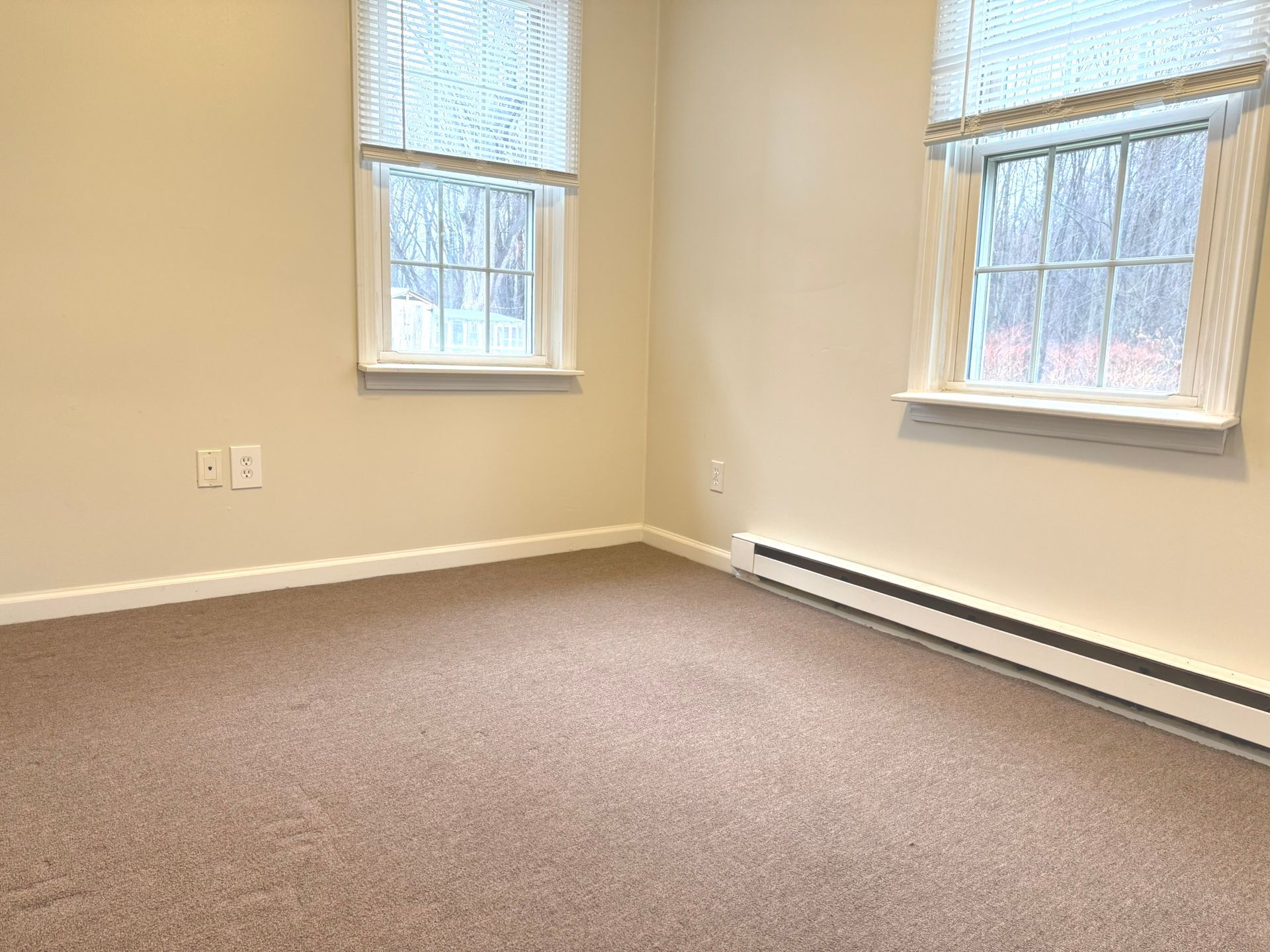 An empty room with two windows and a carpeted floor.