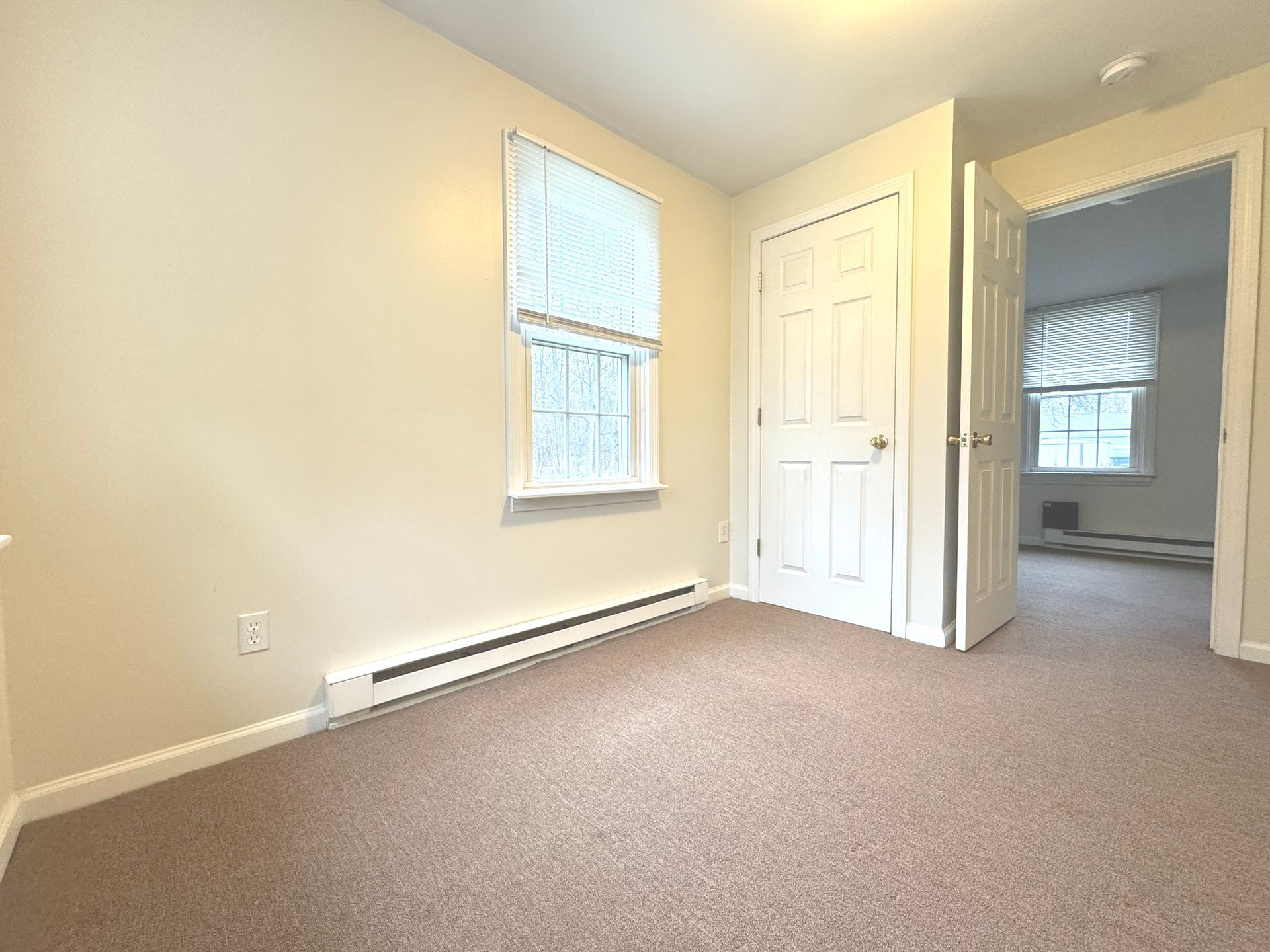 An empty bedroom with a carpeted floor and a window.