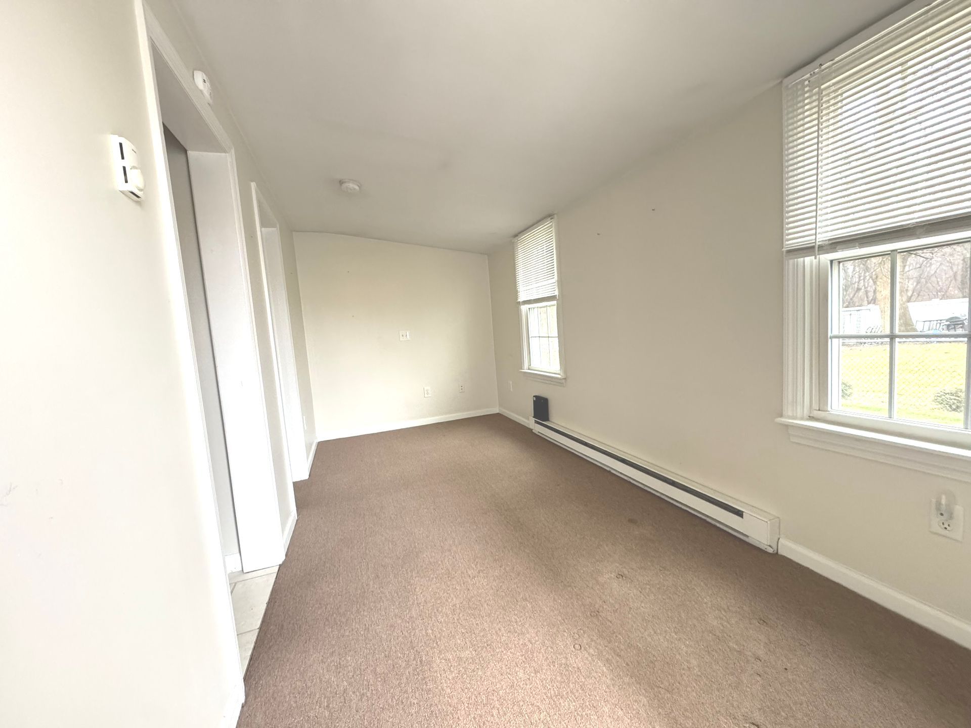 An empty living room with a brown carpet and two windows.