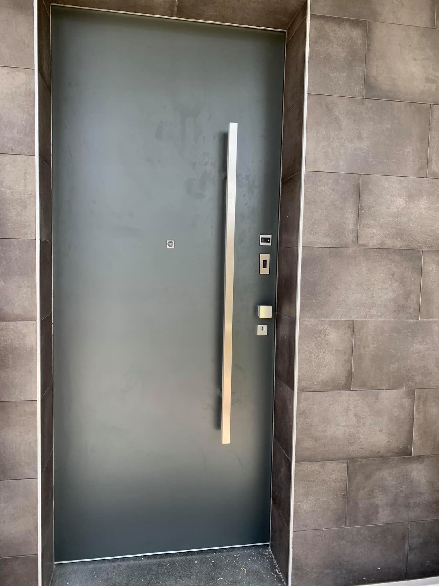 Porta grigia con una lunga maniglia argentata, incastonata in un muro di pietra.