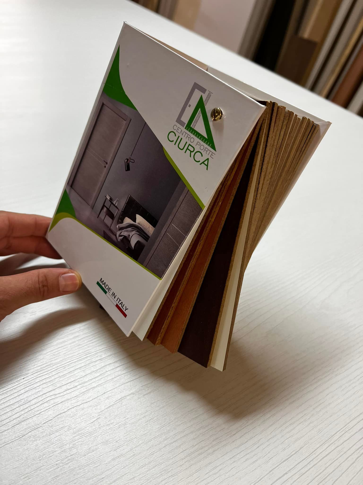 Mano che regge un libretto di campioni di finiture per il legno; tavolo bianco.