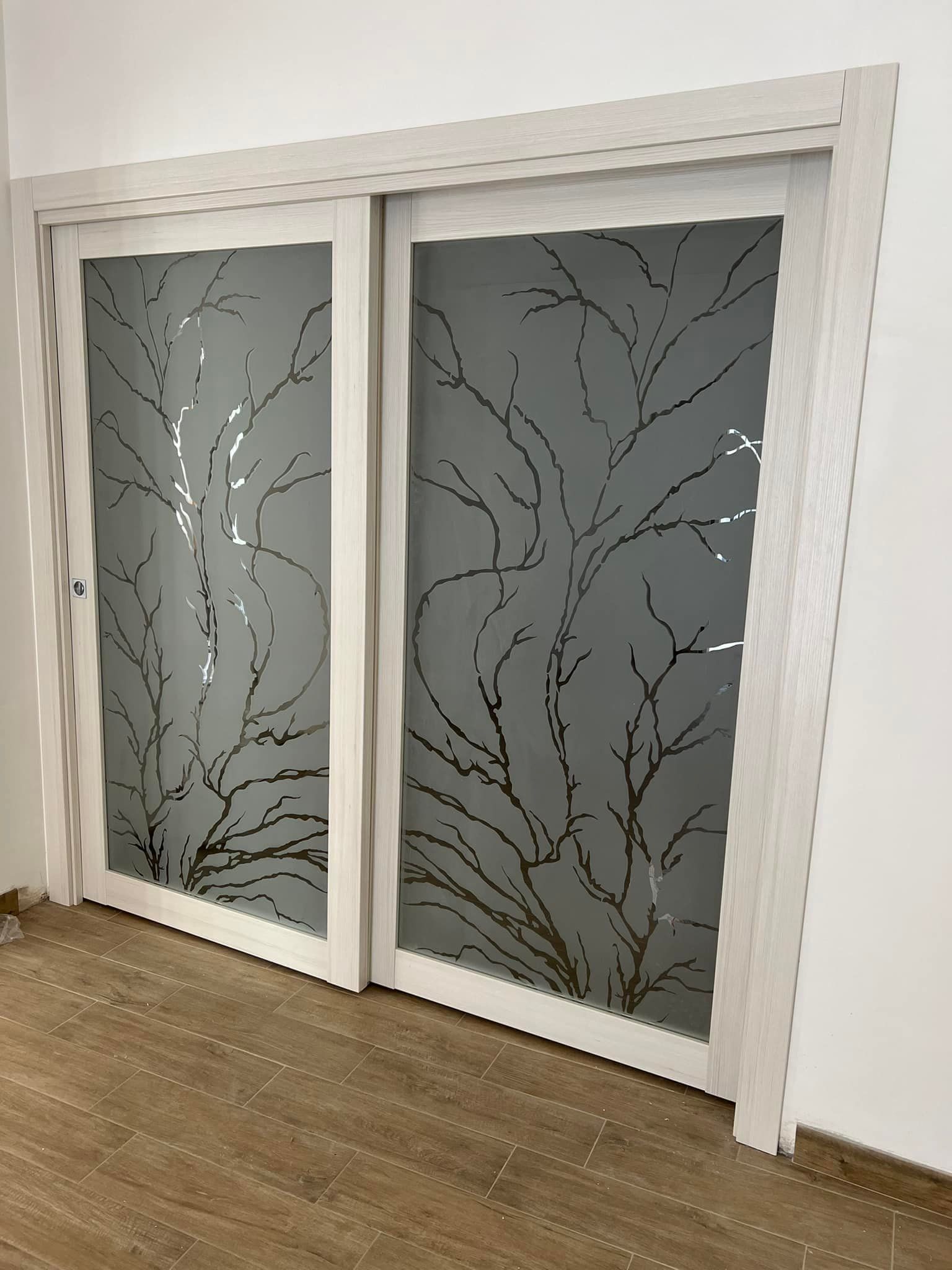 Due porte scorrevoli bianche con motivo inciso a rami d'albero.