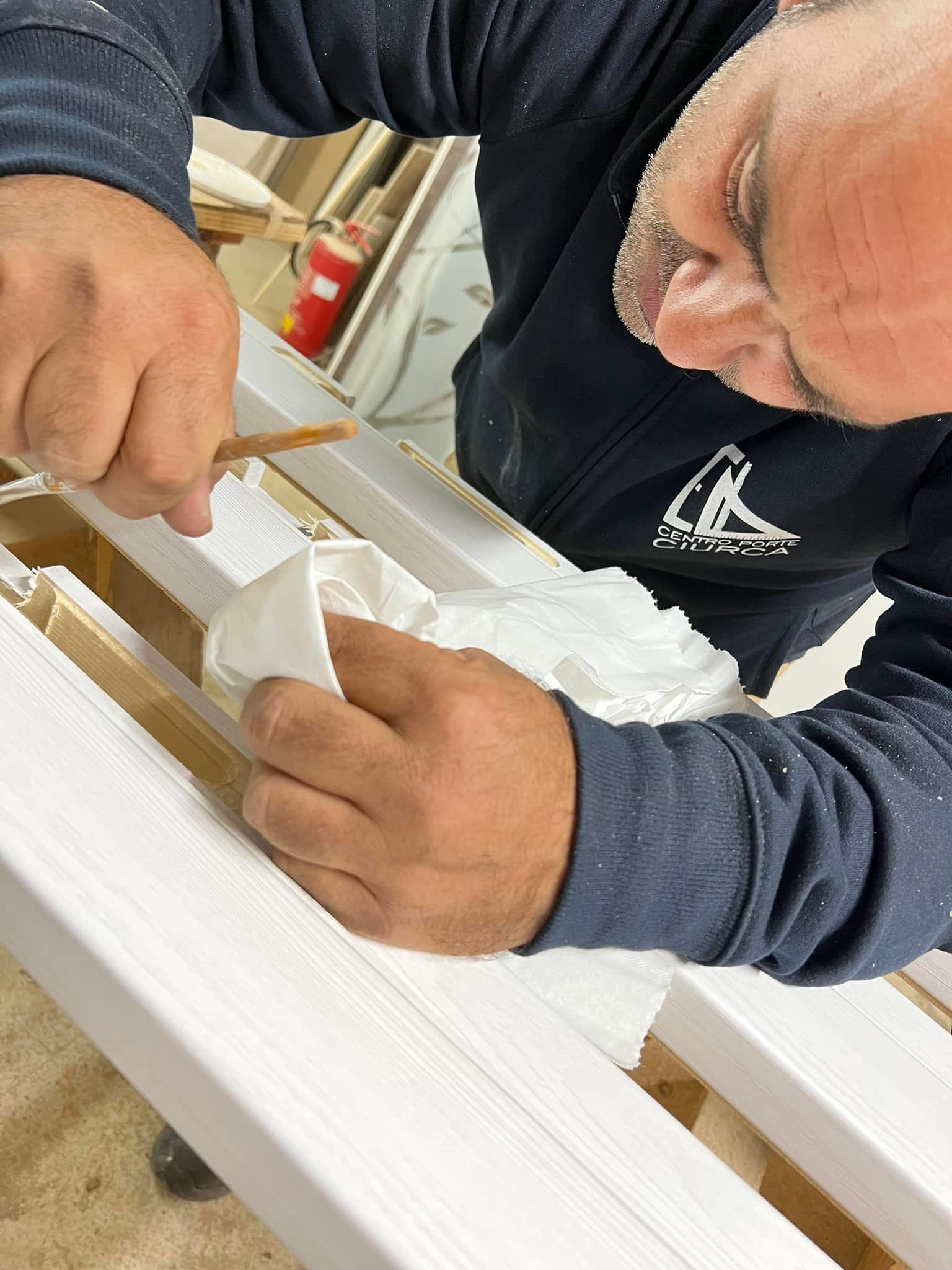 Persona che applica qualcosa su una rifinitura bianca con un attrezzo e un panno su un banco da lavoro.