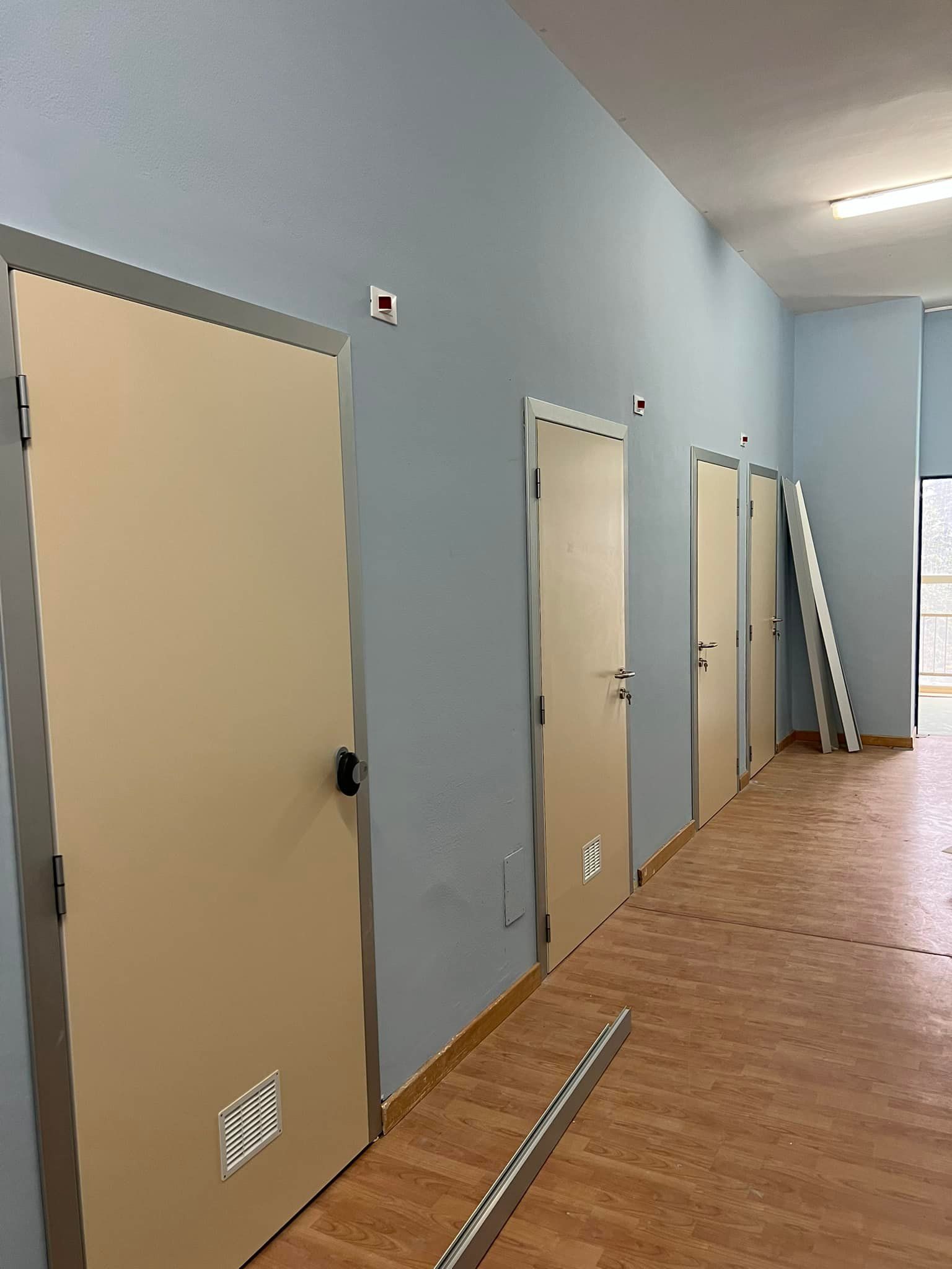 Corridoio con quattro porte color cuoio, pareti blu e pavimento effetto legno.