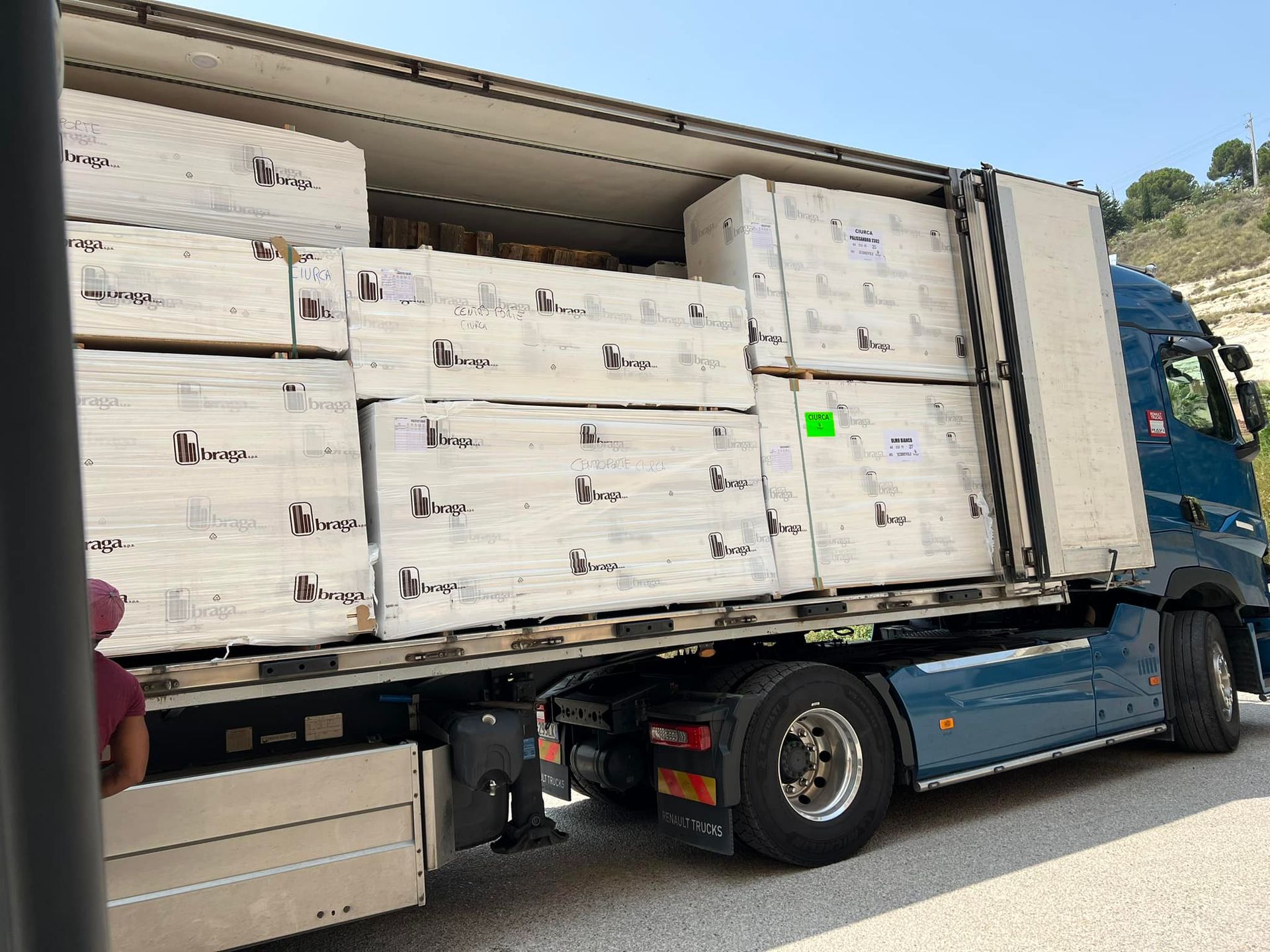 Un semirimorchio blu carico di pacchi bianchi rettangolari, parcheggiato su una strada.