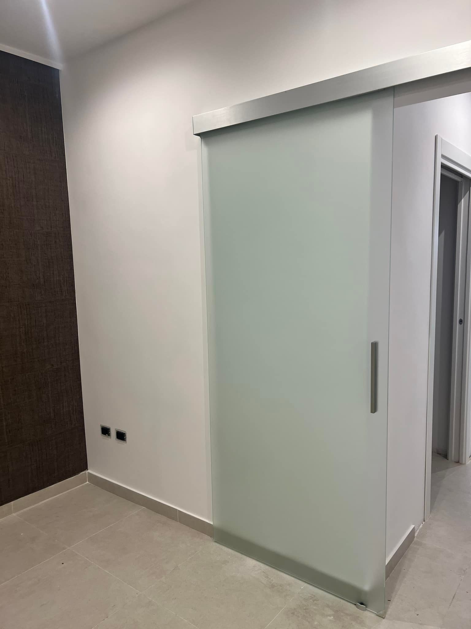 Porta scorrevole in vetro smerigliato in una stanza moderna con pareti bianche e una parete decorativa marrone.
