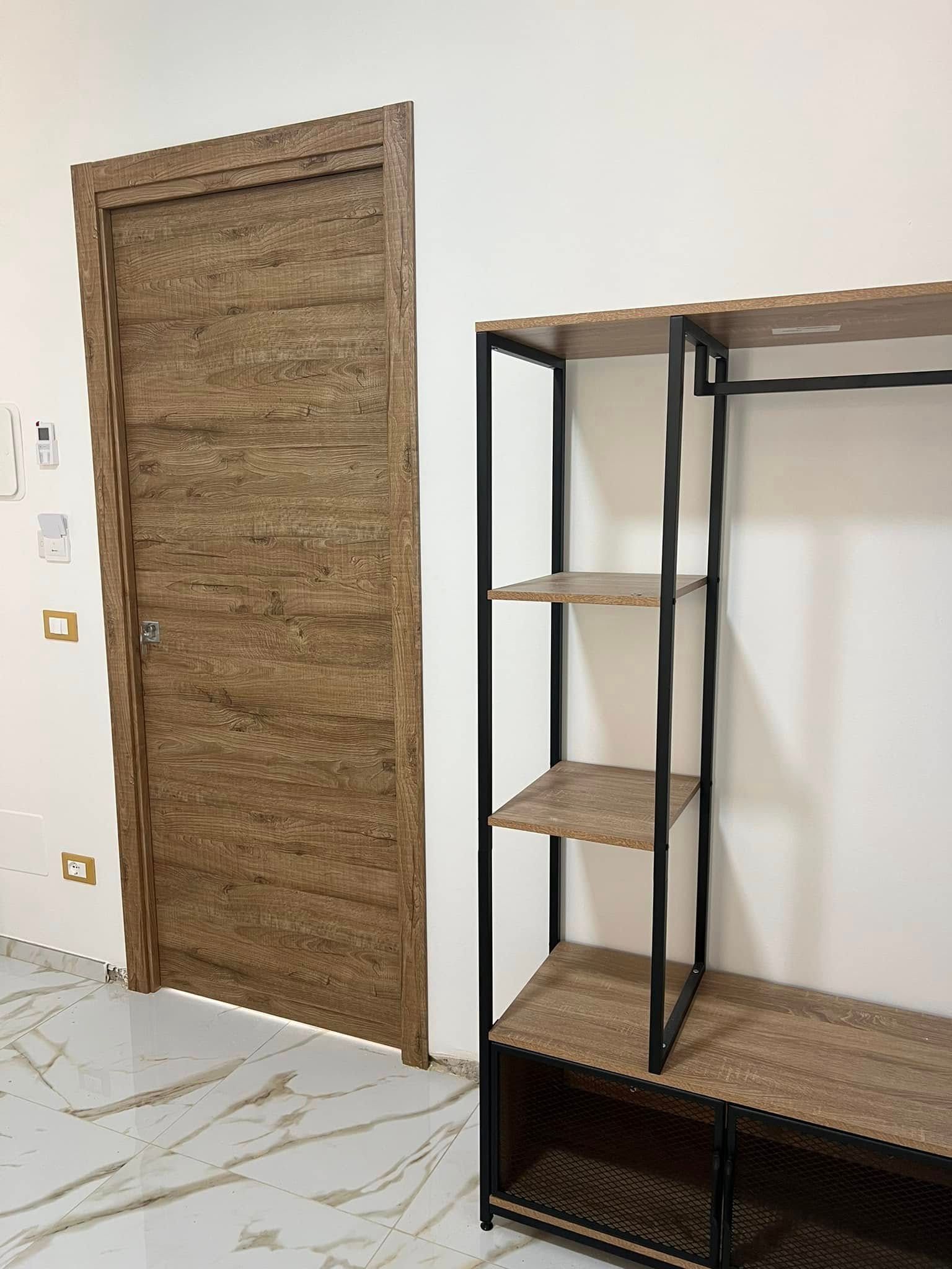 Porta marrone accanto a uno scaffale aperto con cornice nera su una parete bianca.