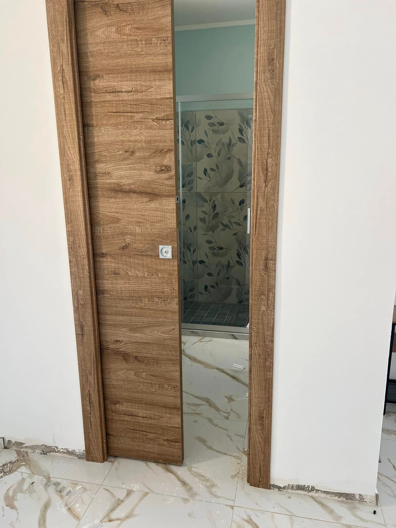 Porta scorrevole in legno parzialmente aperta, che rivela un bagno con box doccia in vetro.