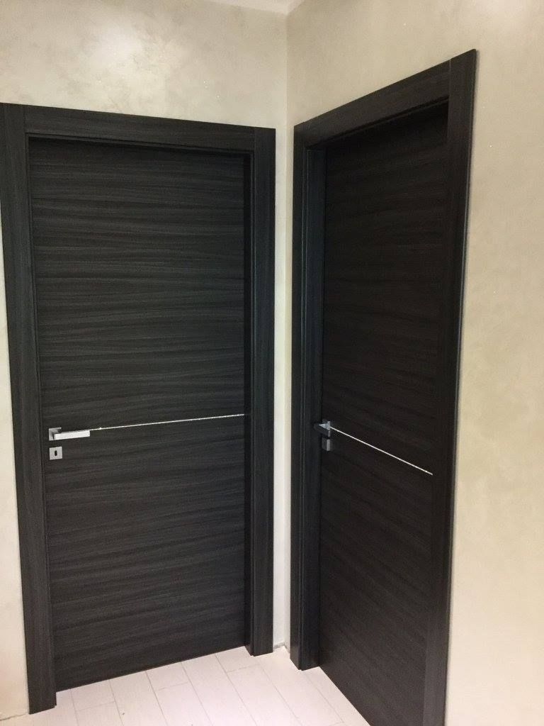 Due porte in legno scuro con maniglie argentate in una stanza dai colori chiari.