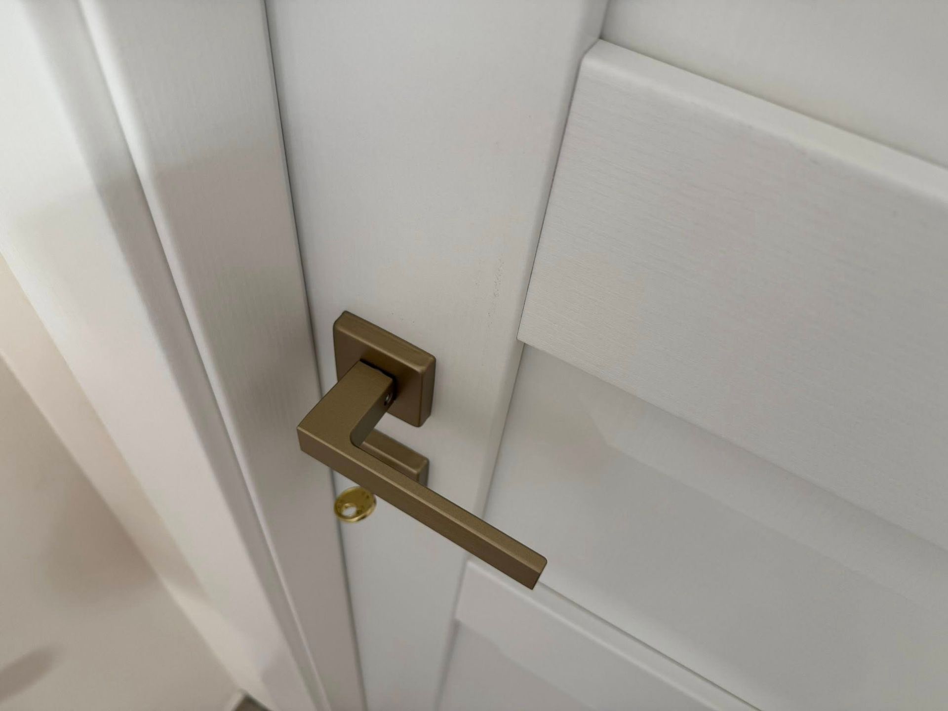 Maniglia in bronzo su una porta bianca. Una chiave è inserita.