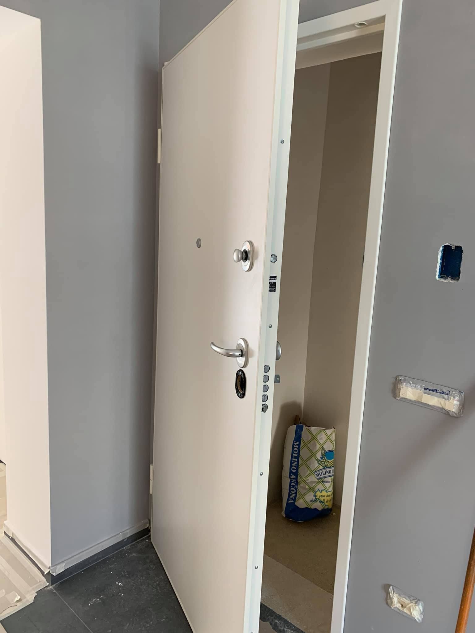 Porta bianca socchiusa, che rivela uno spazio stretto; pareti e stipite della porta grigi.