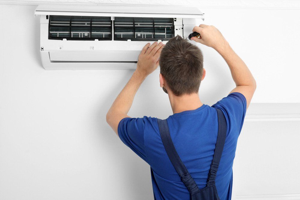 Male Technician In Blue Uniform Installing Split Type Aircon — Servicing Homes & Businesses in Wollongong