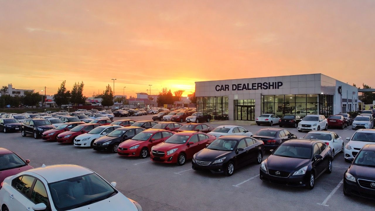 Cars parked in front of a dealership building under a sunset sky.