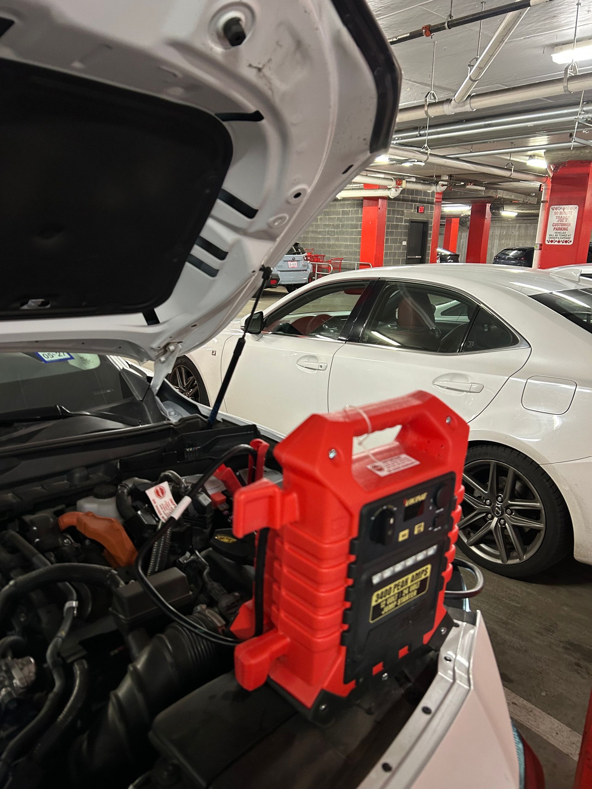 Red portable jump starter clipped to a car battery in an auto repair garage, with a white car nearby
