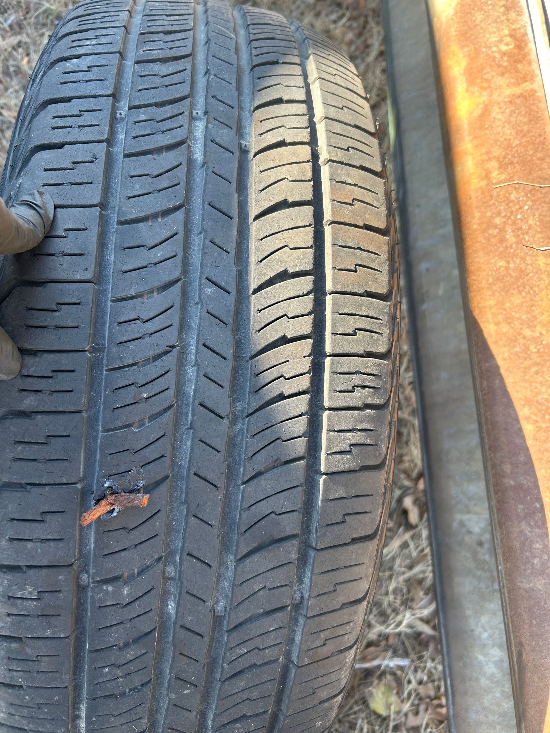 Close-up of a worn car tire tread with a small puncture or tear near the center.