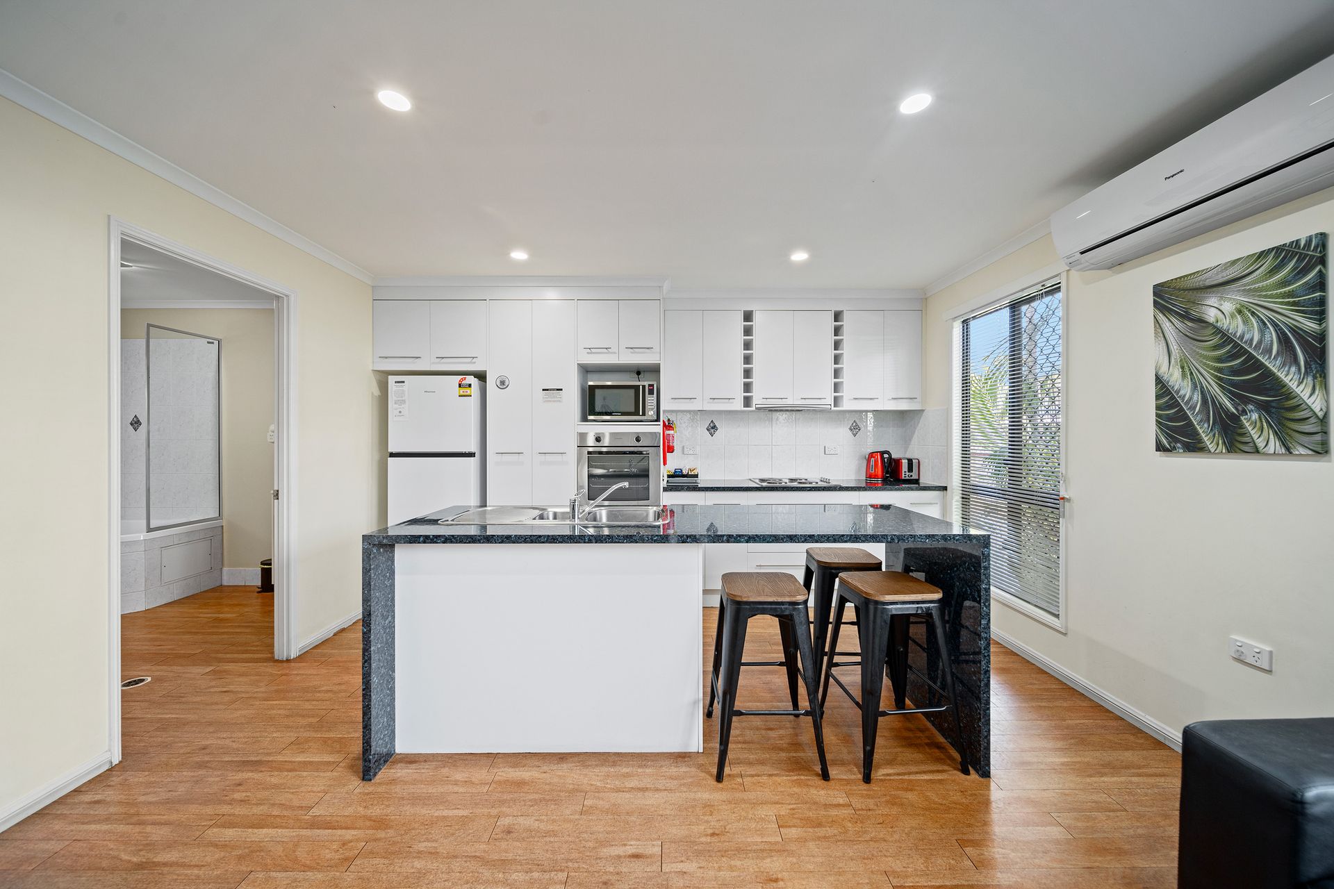 A kitchen with a large island and stools in a living room.