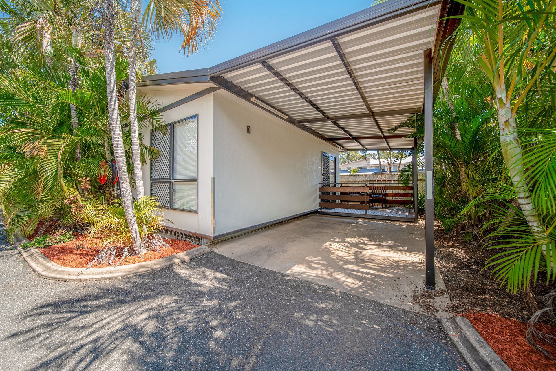 A white house with a carport in front of it surrounded by trees.