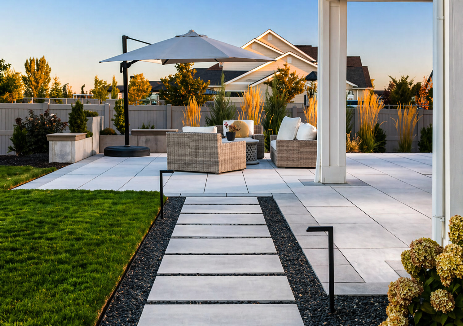 Modern backyard patio with white stone path, green lawn, and outdoor seating under a large umbrella