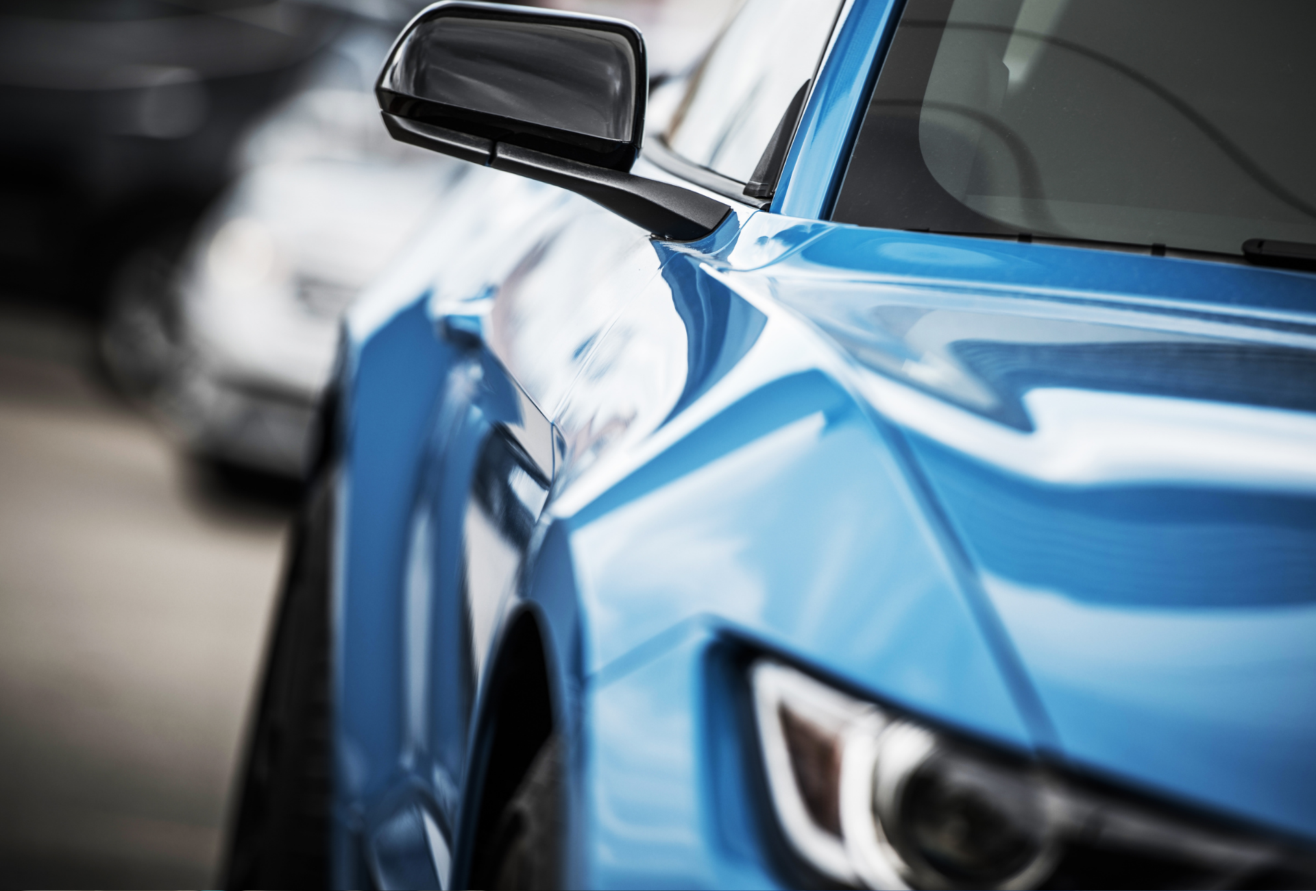 Blue sports car, close-up of the front fender and side mirror, parked in a row with other vehicles.